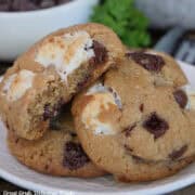 Three brown butter s'mores cookies on a white plate with a bite out of one of the cookies.