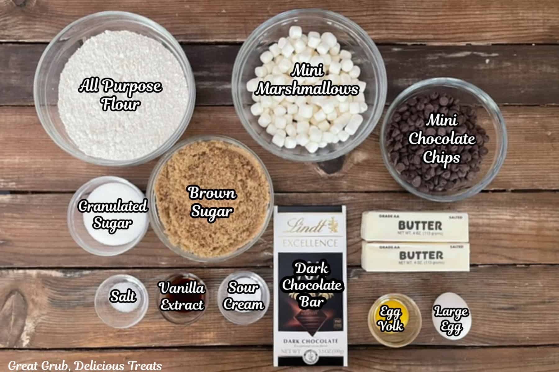 A rustic wood surface with all the ingredients placed on it to make brown butter s'mores cookies.