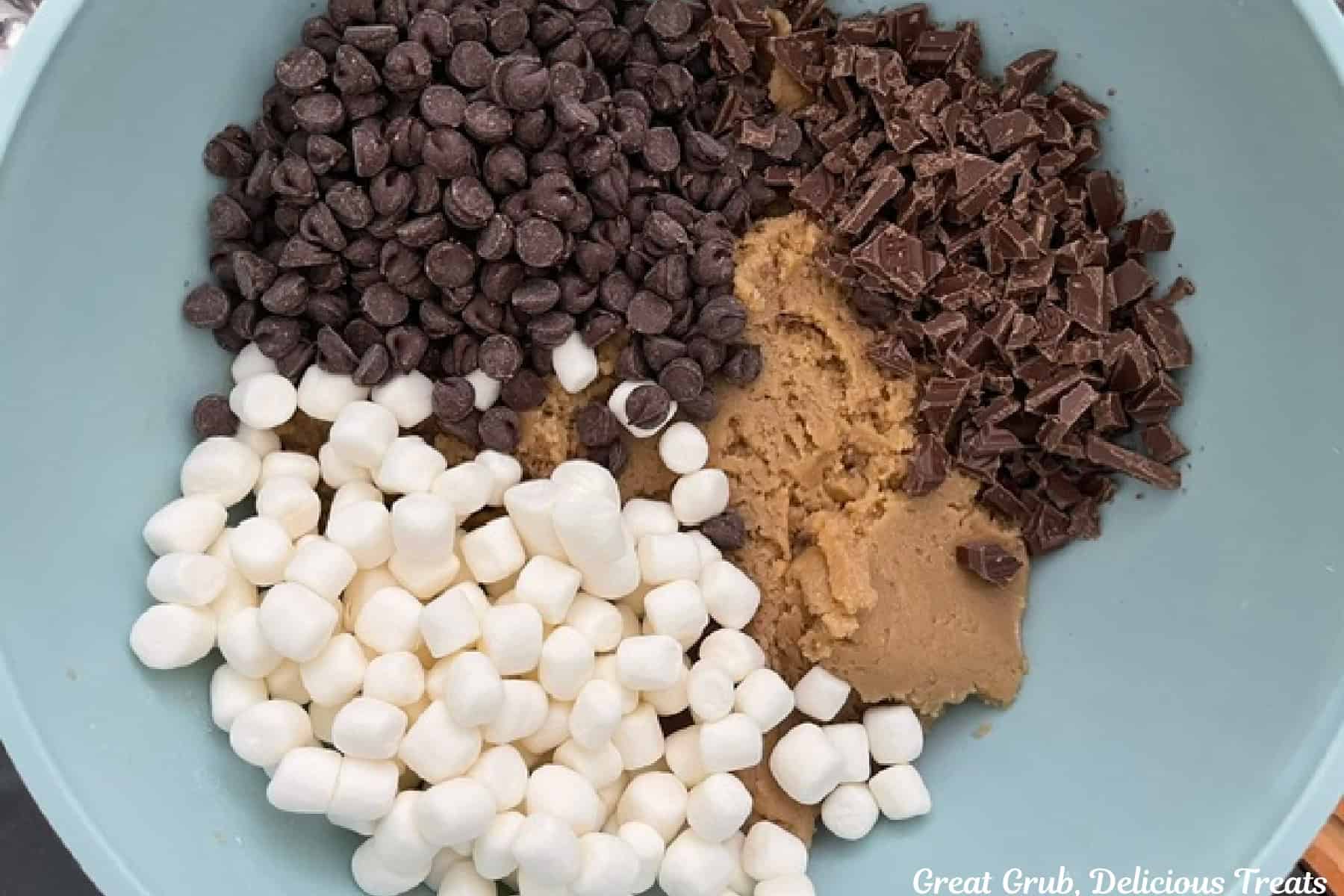 A mixing bowl with the brown butter cookie dough and mini marshmallows, mini chocolate chips, and dark chocolate added before being combined.