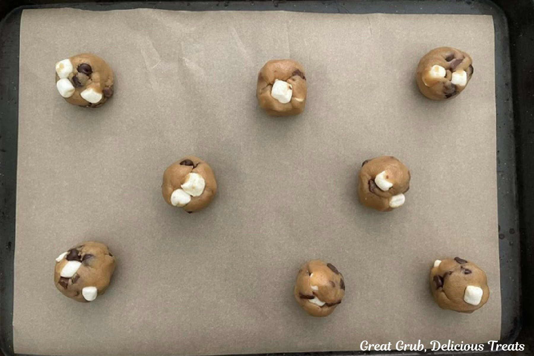 A baking sheet lined with parchment paper with eight cookie dough balls on it before being baked.