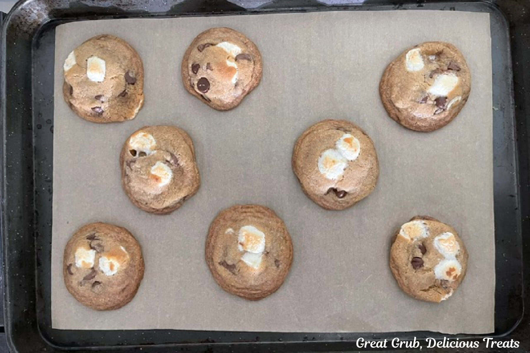 A parchment lined baking sheet with eight baked brown butter s'mores cookies on it.