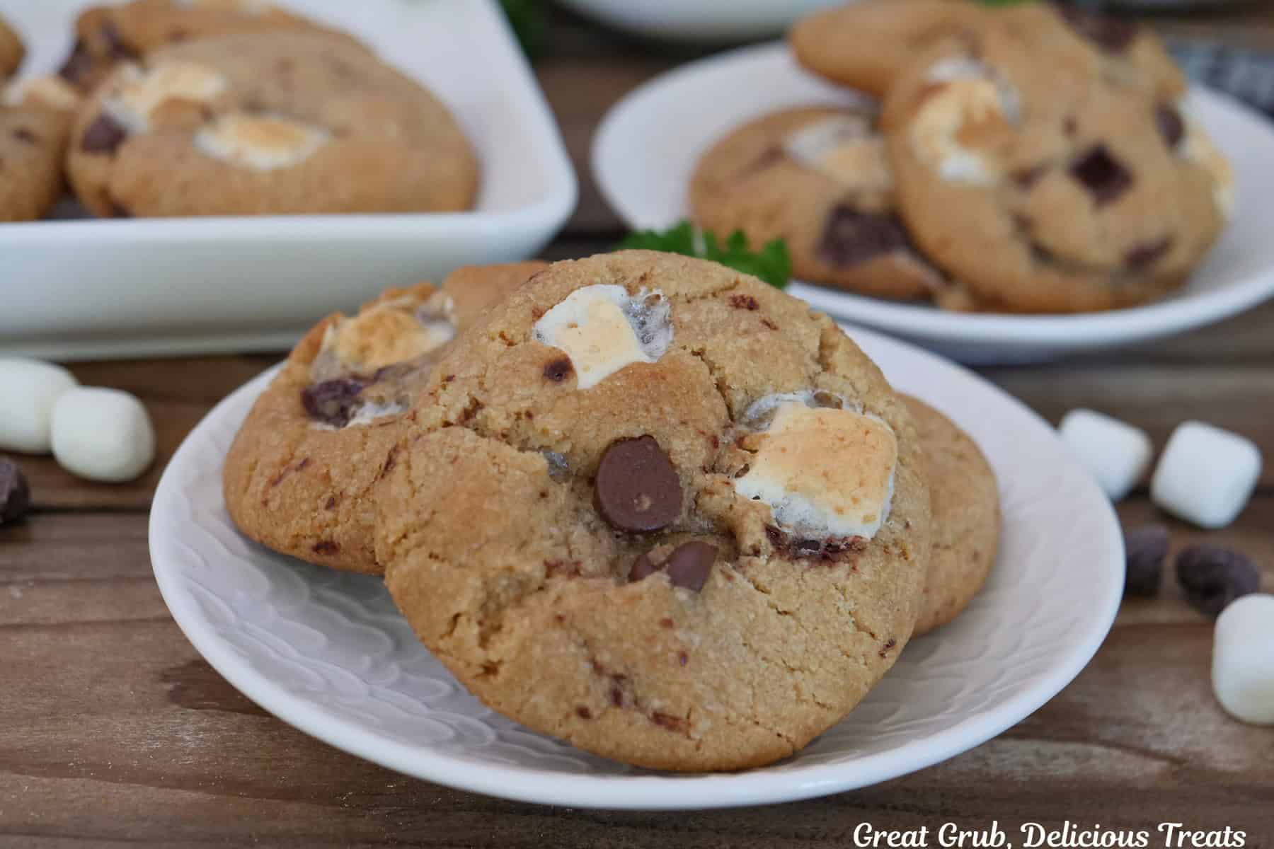 A wood surface with three white plates with brown butter s'mores cookies on them.