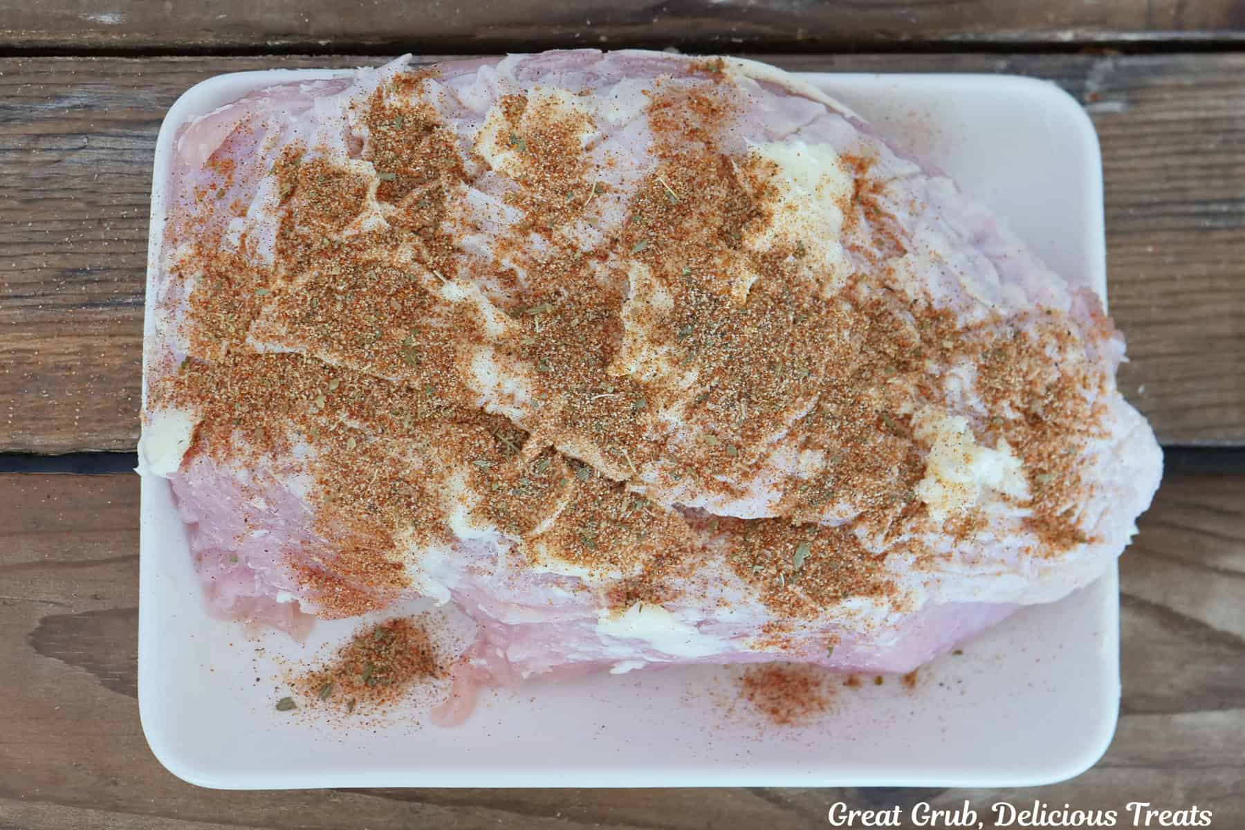 A white plate with a turkey breast roast on it covered in butter and topped with a zesty blend of seasonings before being smoked.