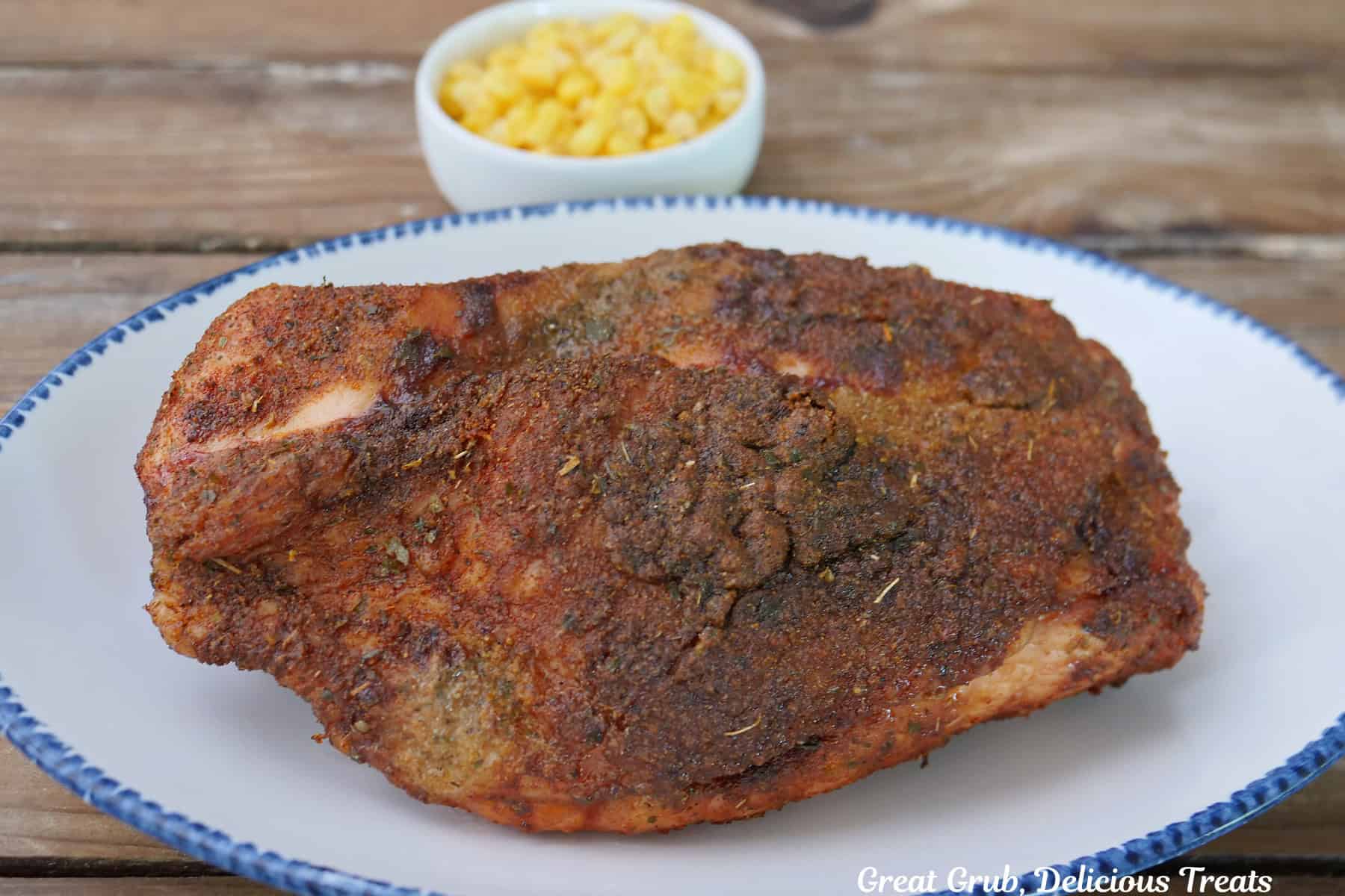 A wood surface with a white oval blue trimmed white plate with the whole smoked Cajun turkey breast on it before being sliced.