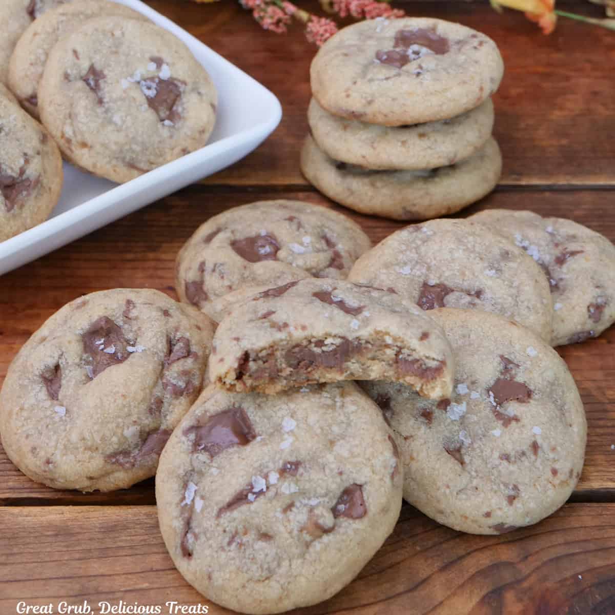 A wood surface with a dozen chocolate caramel cookies on it with a bite taken out of one of the cookies.