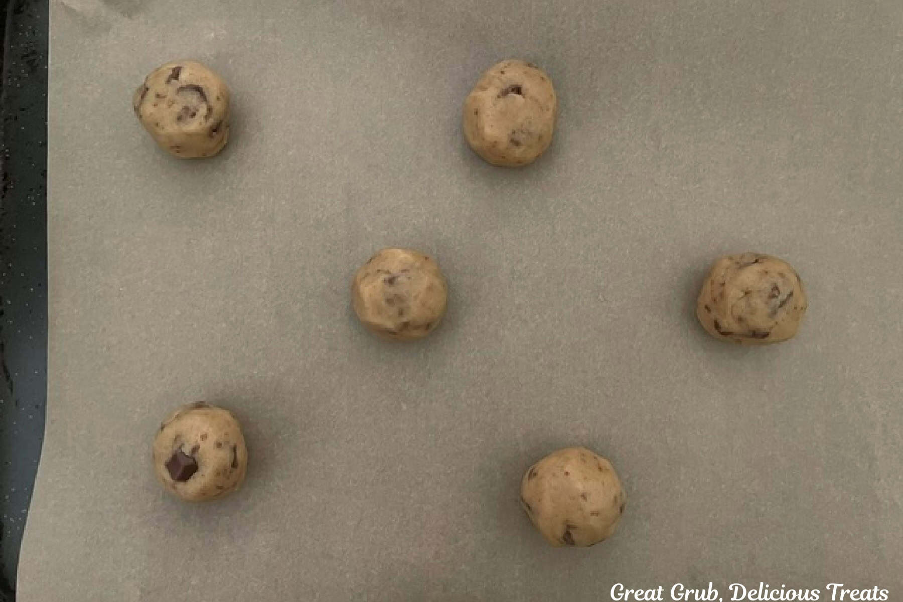 A parchment lined baking sheet with six cookie dough balls on it.