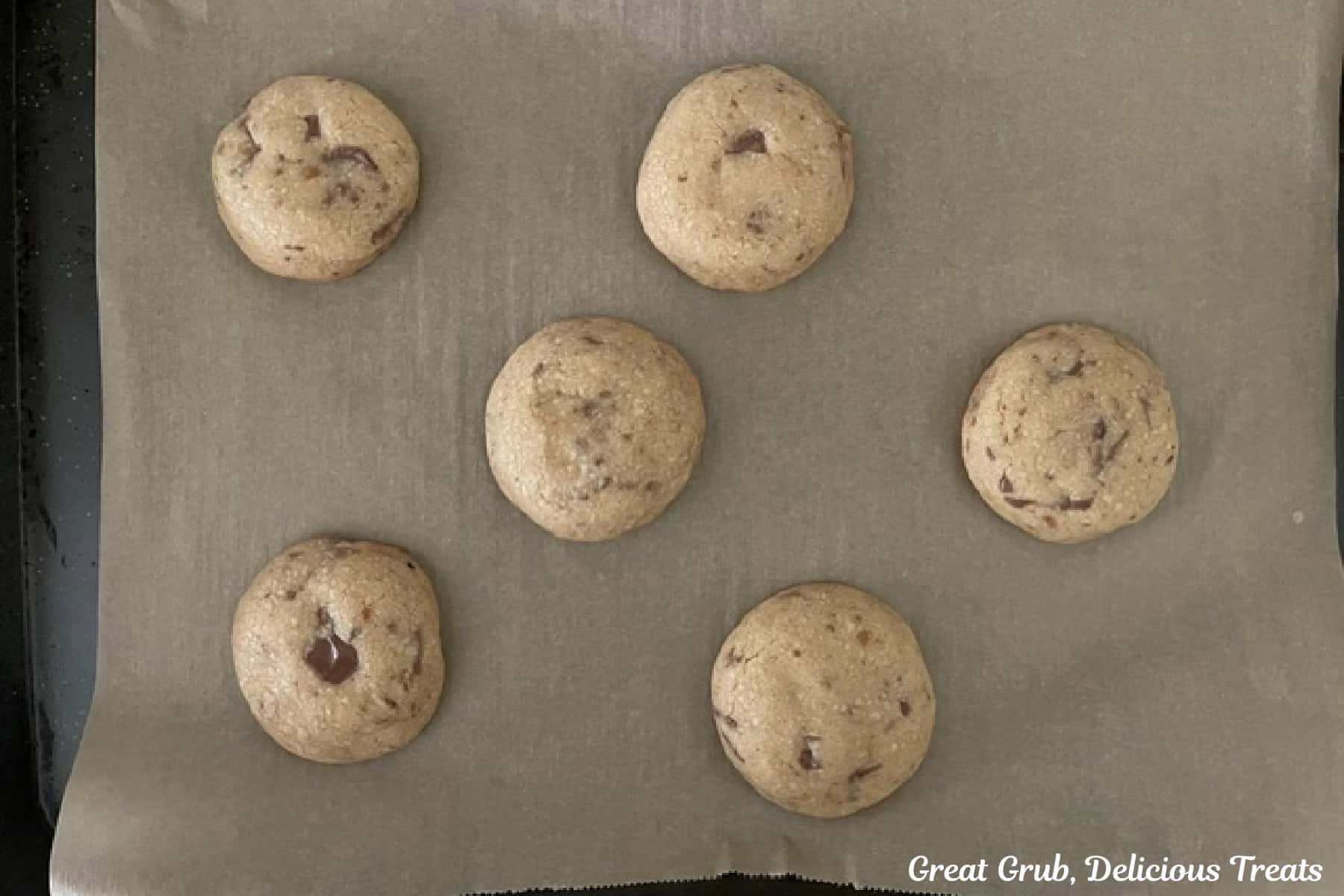 A parchment lined baking sheet with six cookies on it that were just removed from the oven.