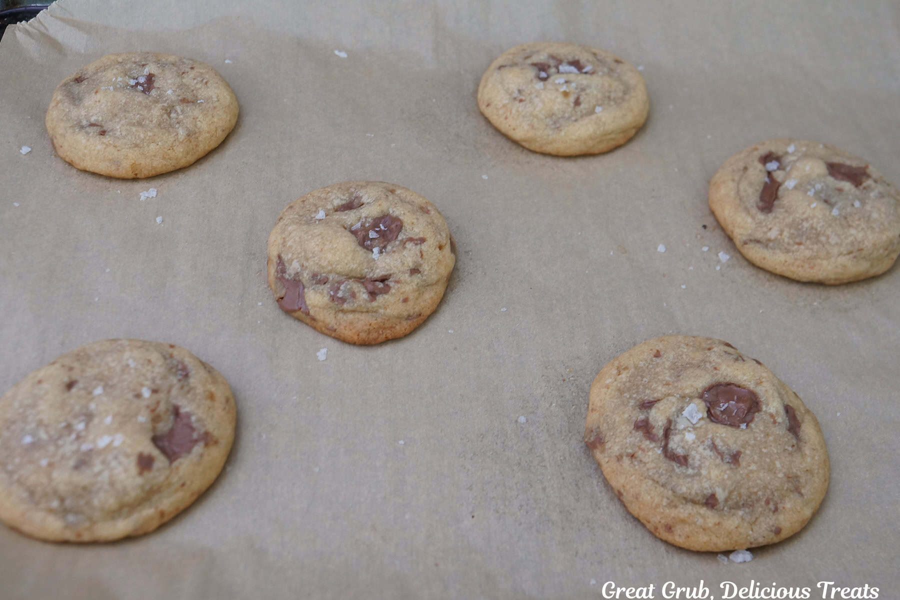 A baking sheet lined with parchment paper with six chocolate caramel cookies on it after being sprinkled with sea salt.