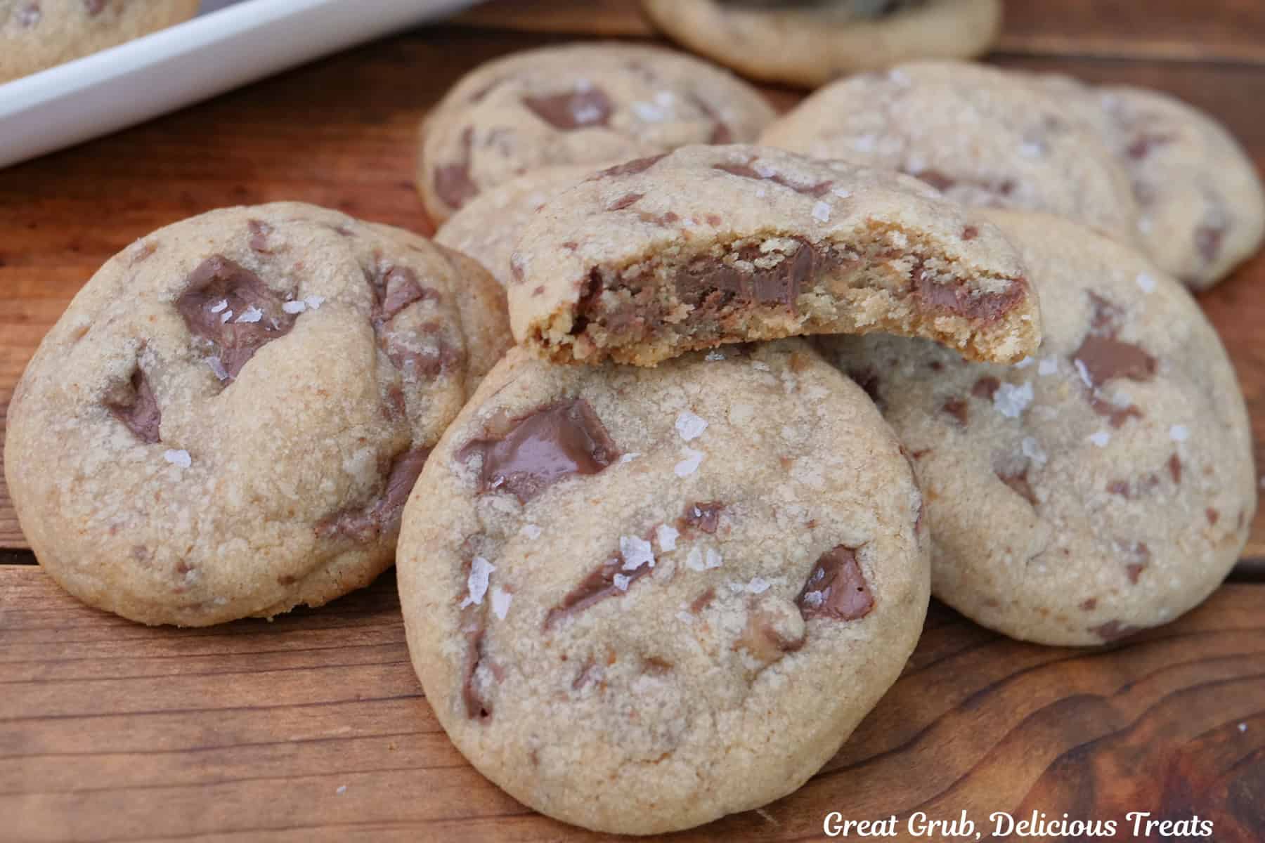 A wood surface with seven chocolate caramel cookies placed on it with a bite taken out of the cookie on top.