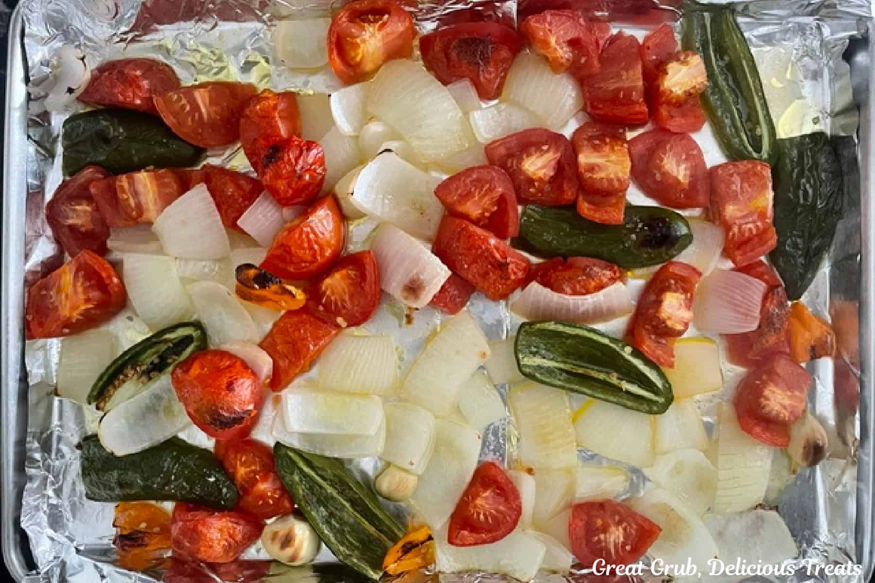A baking sheet with roasted onions, tomatoes, and three types of peppers on it.