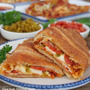 A white plate with blue trim with a pepperoni pizza croissant sandwich that is cut in half placed on it.