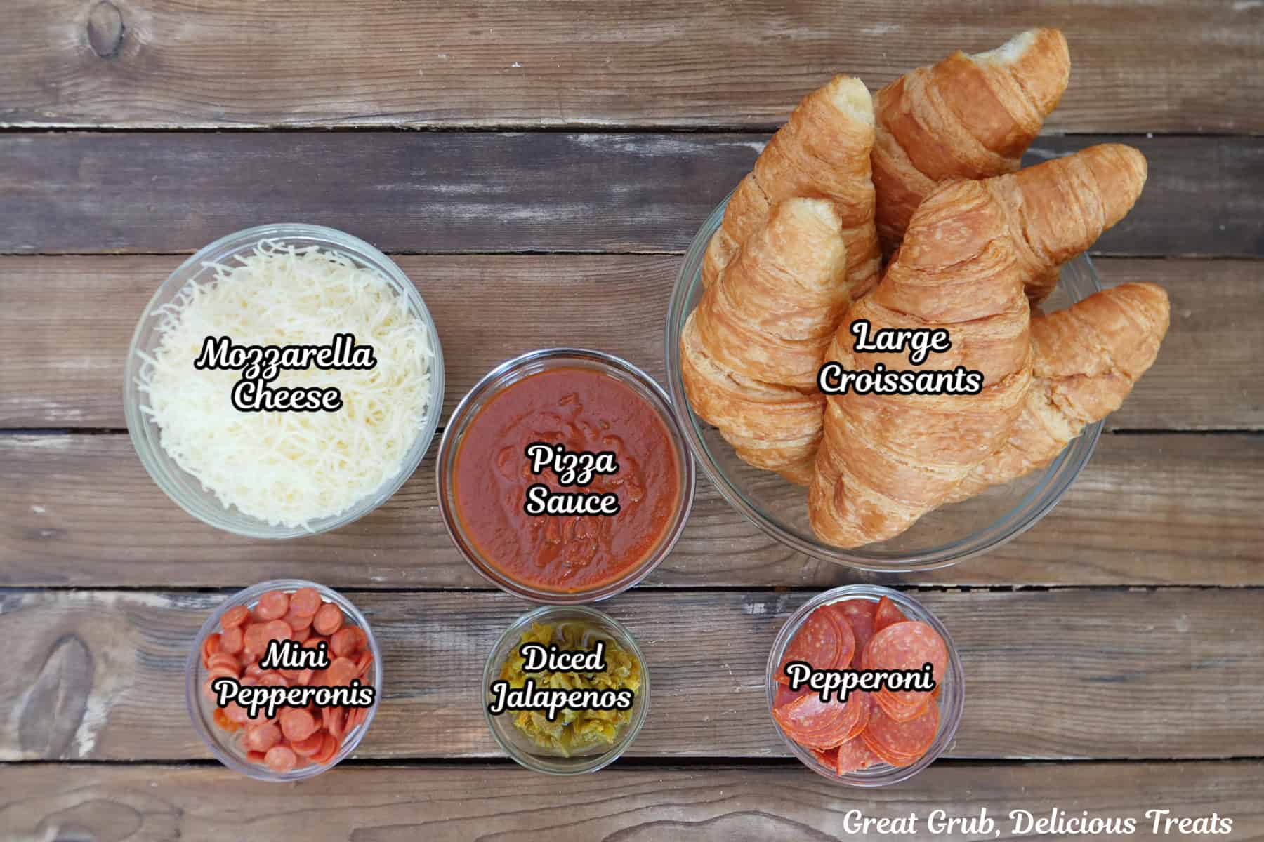 A woos surface with all the ingredients placed on it to make pepperoni pizza croissant sandwiches.