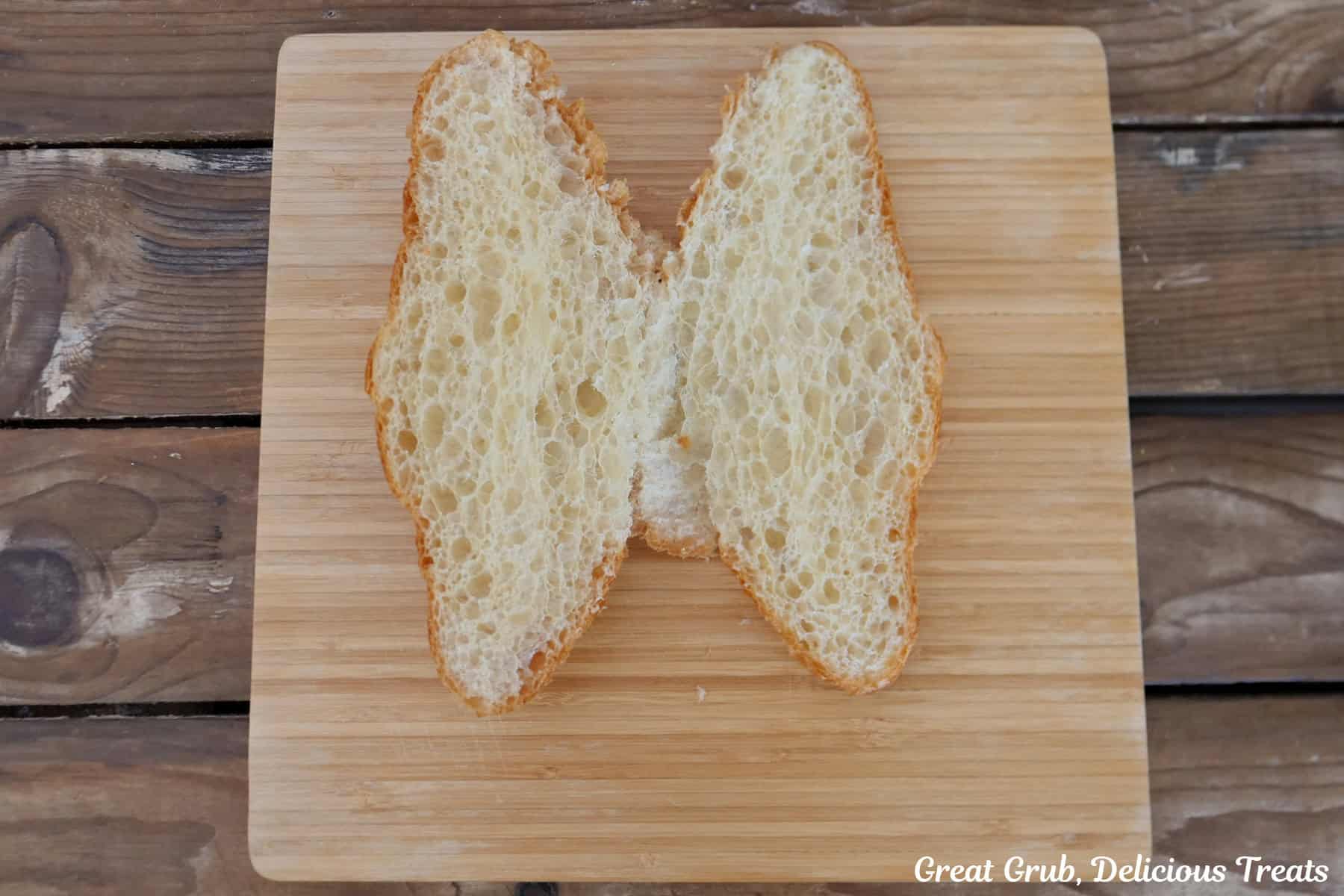 A wood cutting board with a large buttery croissant cut in half with both pieces opened up.