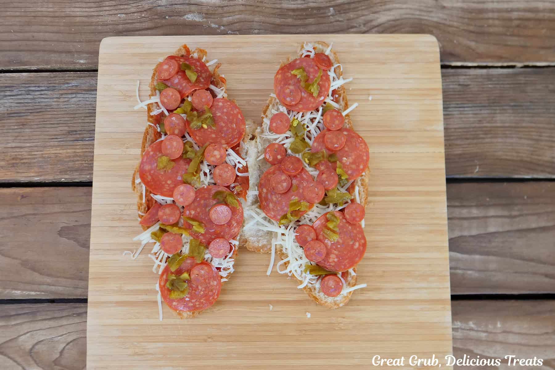 A wood cutting board with a large croissant halved, covered with sauce, pepperonis, cheese, diced jalapenos.