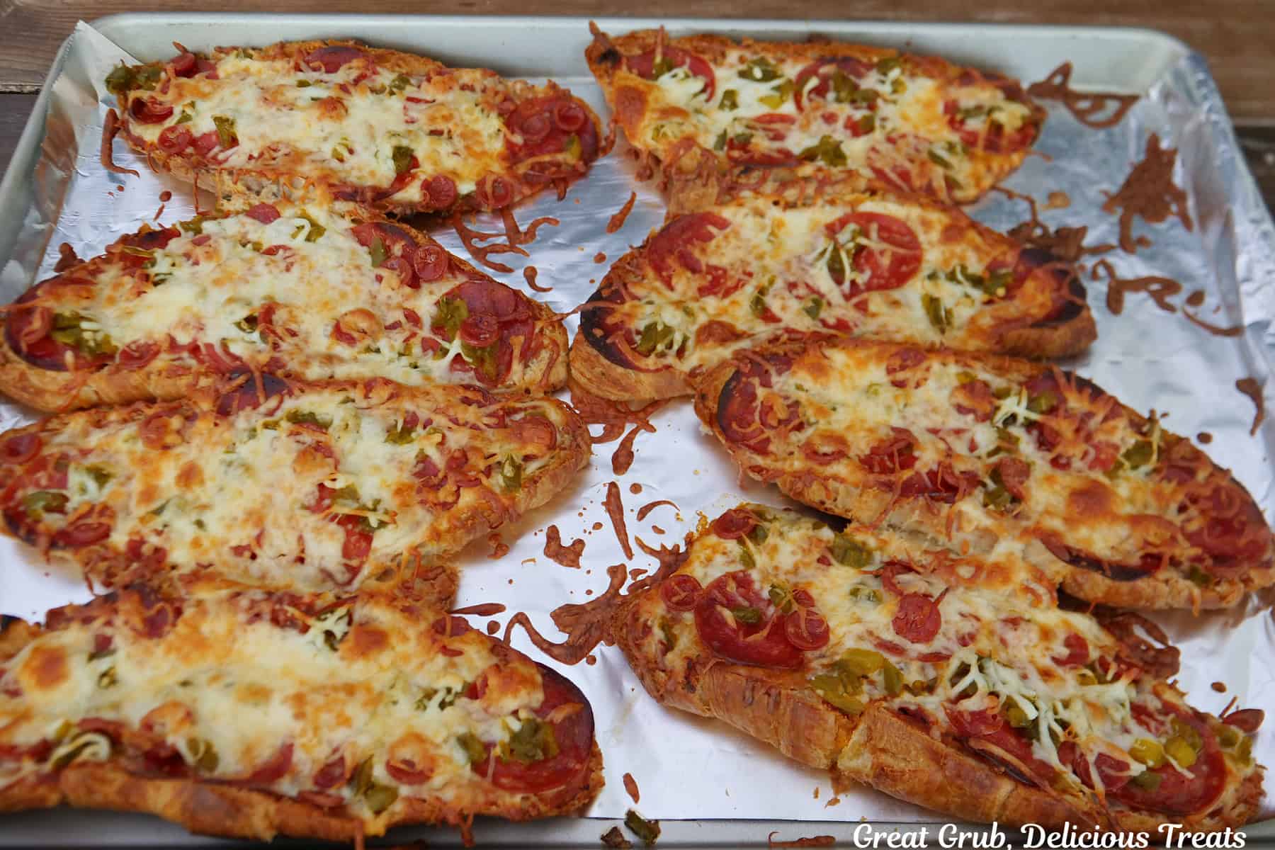 A foil lined baking sheet with eight halves of pepperoni pizza croissants on it after being baked in the oven.