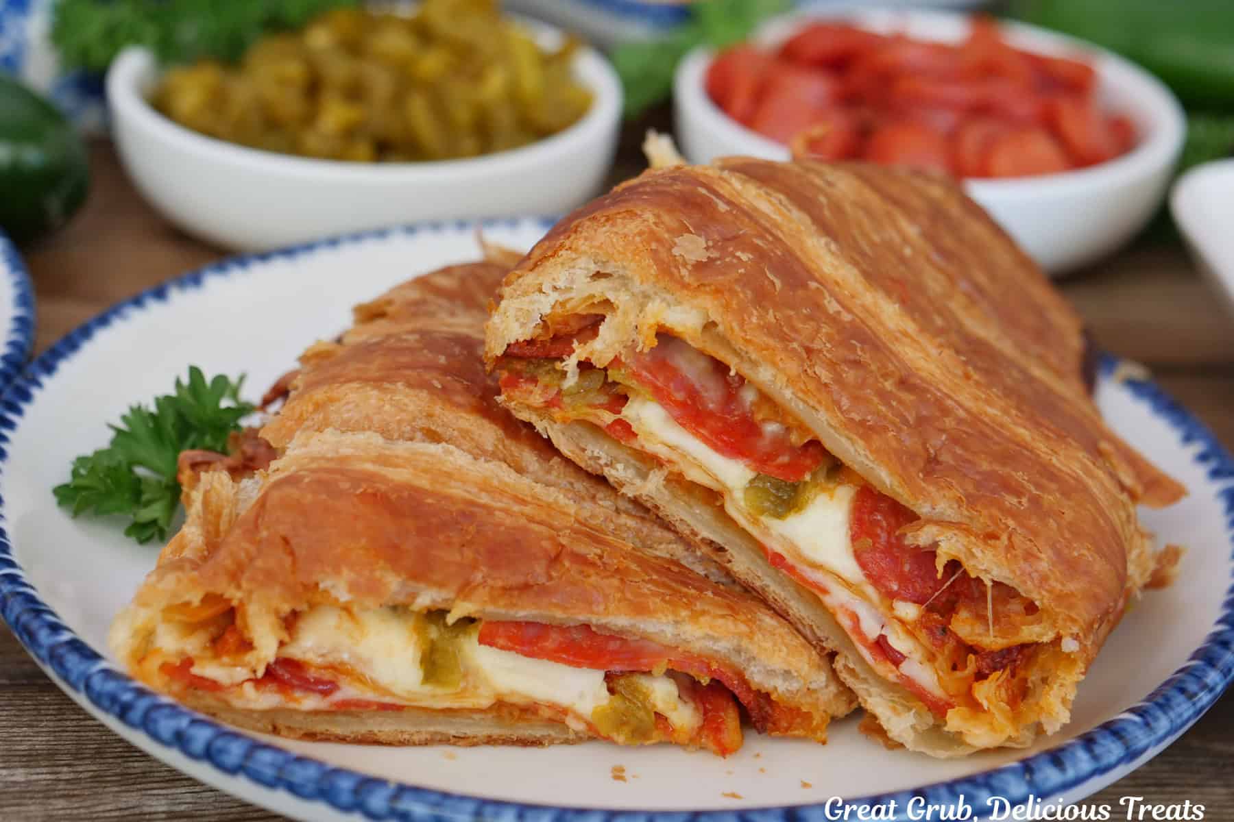 A white plate with blue trim with a pepperoni pizza croissant sandwich cut in half and placed on the plate.