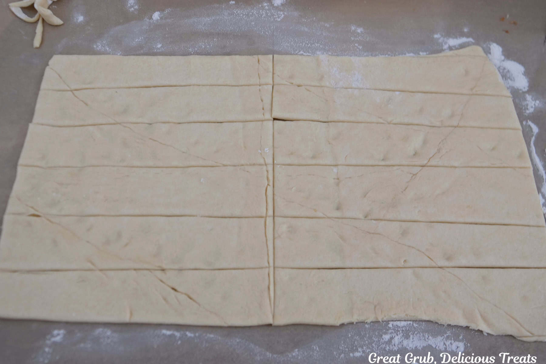 A countertop dusted with flour and a roll of crescent dough rolled out and cut into six strips and then those strips cut in half.