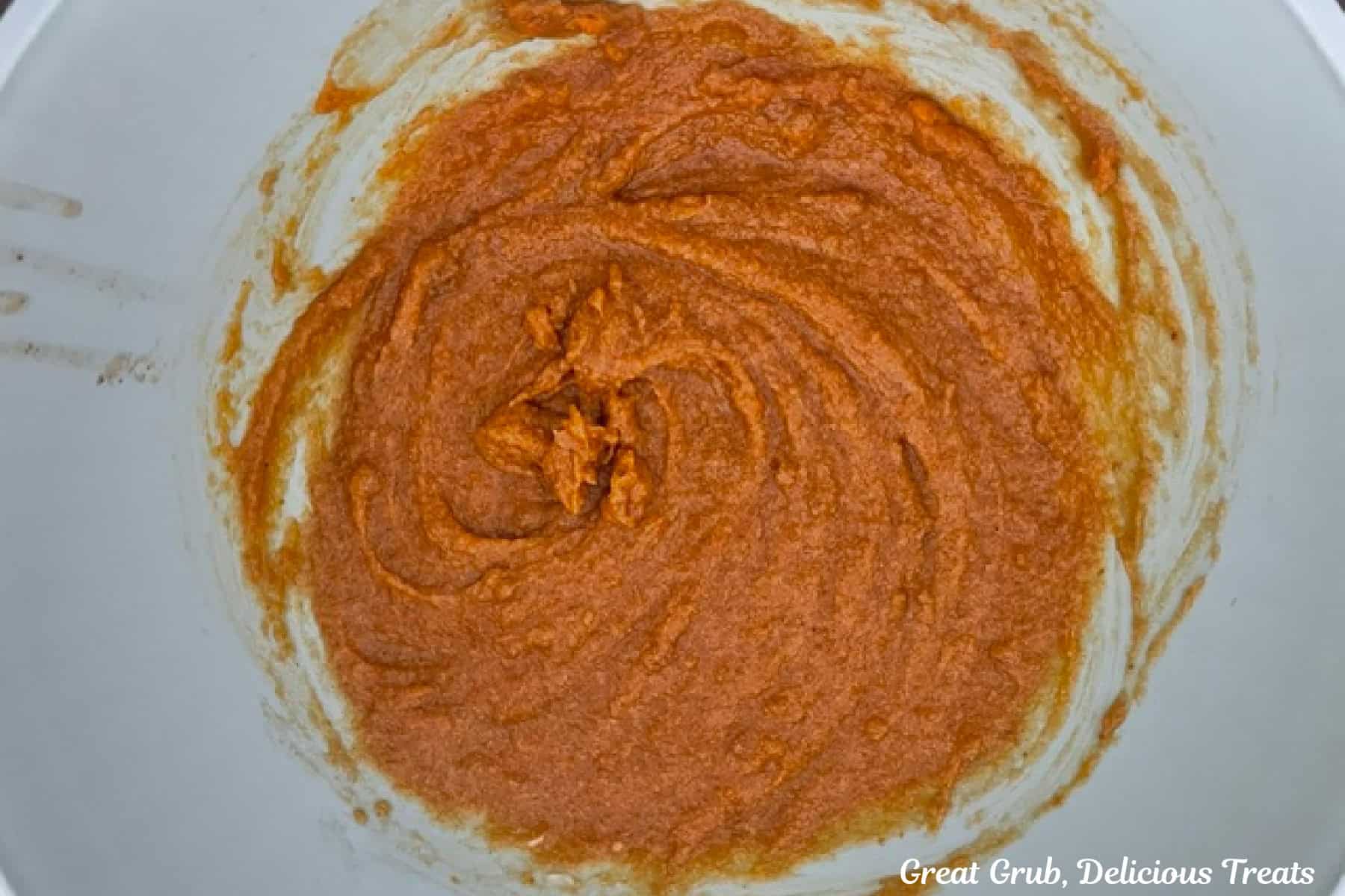 A light colored mixing bowl with the pumpkin cookies wet ingredients mixed together.