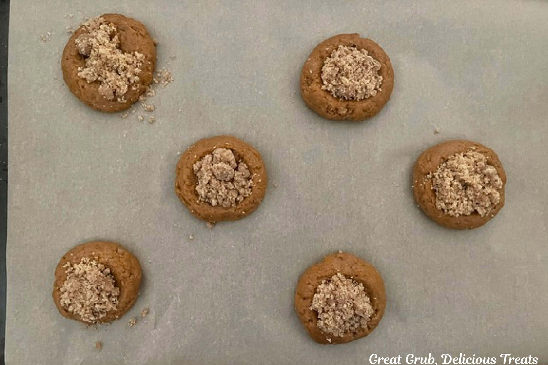 A baking sheet lined with parchment paper with the streusel topping added with the top of the pumpkin cookies.