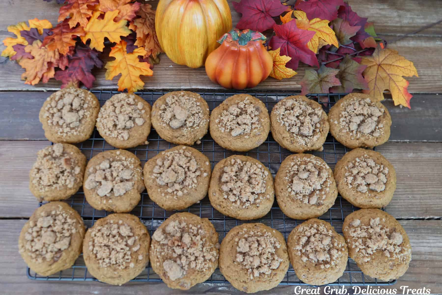 A wood surface with a wire rack placed on it holding eighteen pumpkin streusel cookies cooking on it.