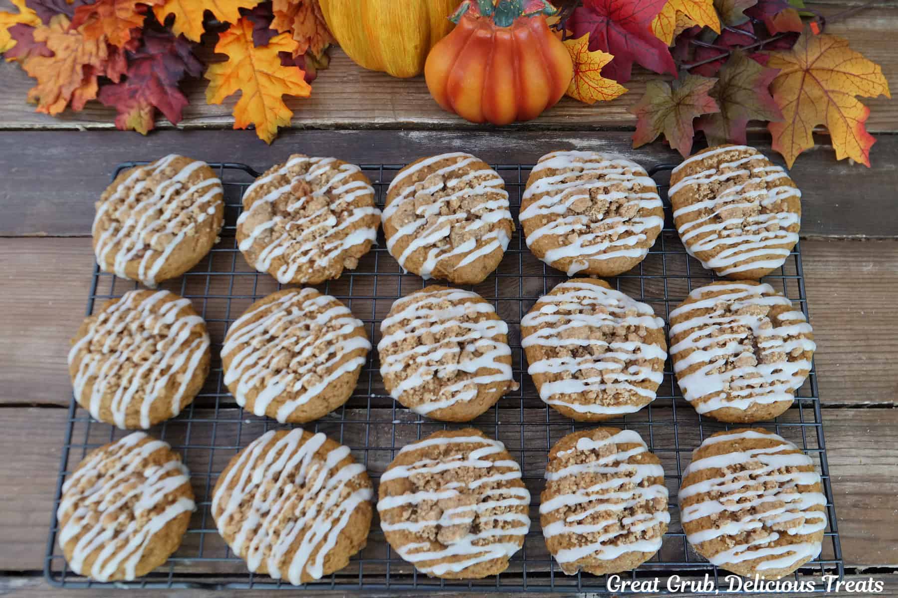 A wood surface with fifteen pumpkin streusel cookies with maple icing on a wire rack.