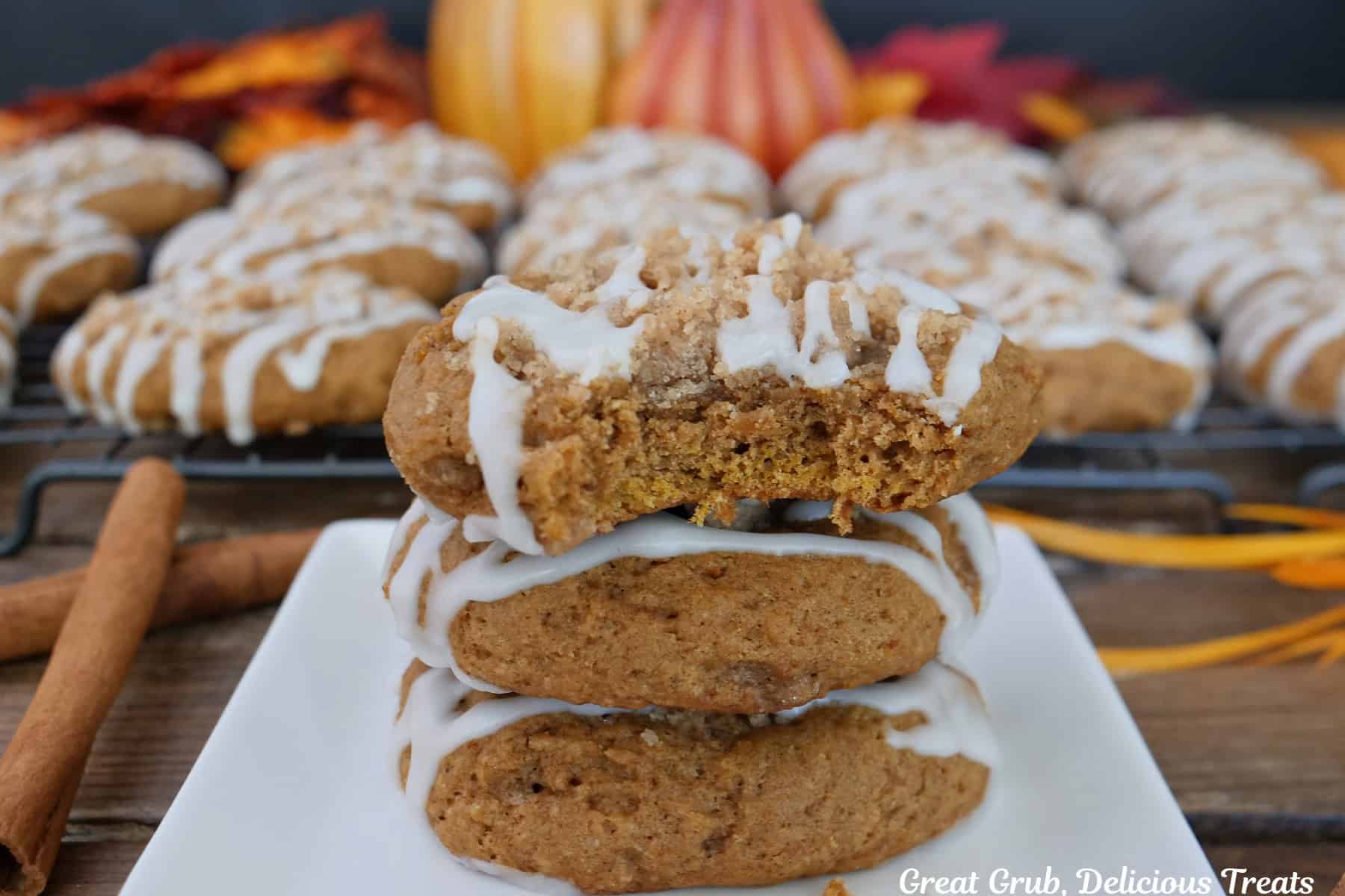 A wood surface with a white plate with three cookies on it and a bite out of the cookie on top, with more cookies in the background.