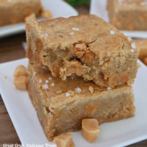 A white plate with two salted caramel blondies on it with a bite taken out of the blondie on top.