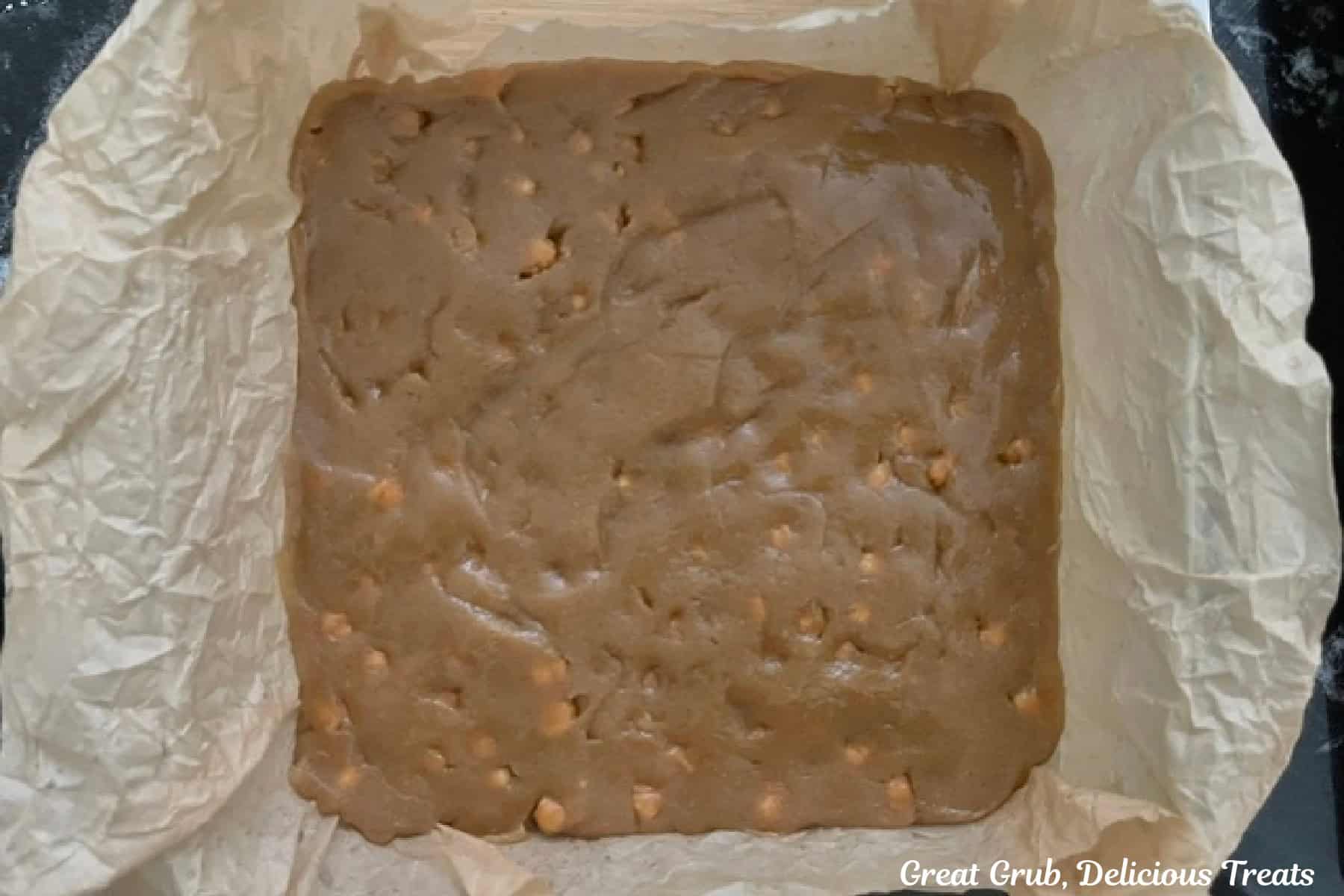 An 8 by 8 baking dish lined with parchment paper with salted caramel blondie batter in it before being baked.