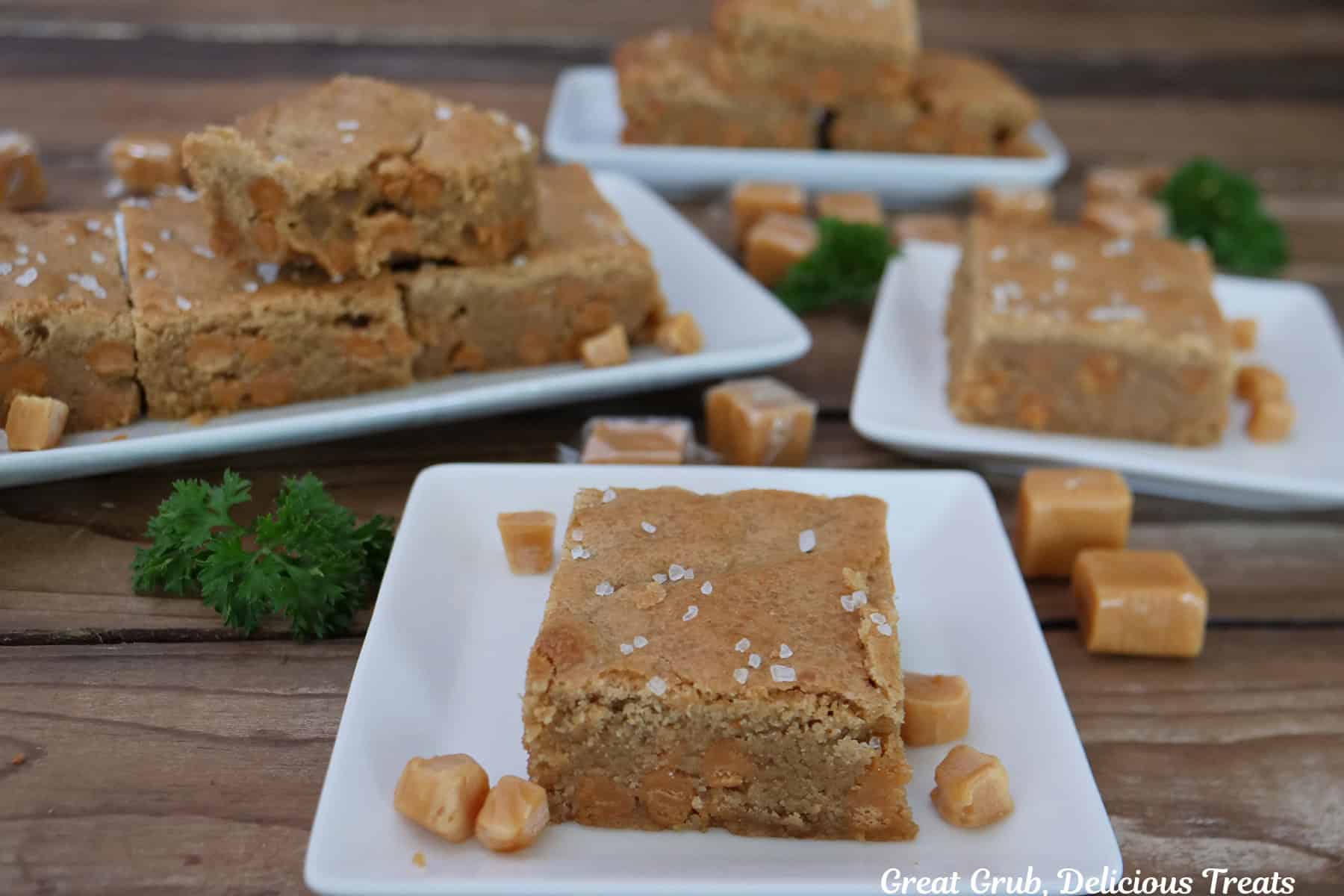 A wood surface with four white plates with salted caramel blondies on them.
