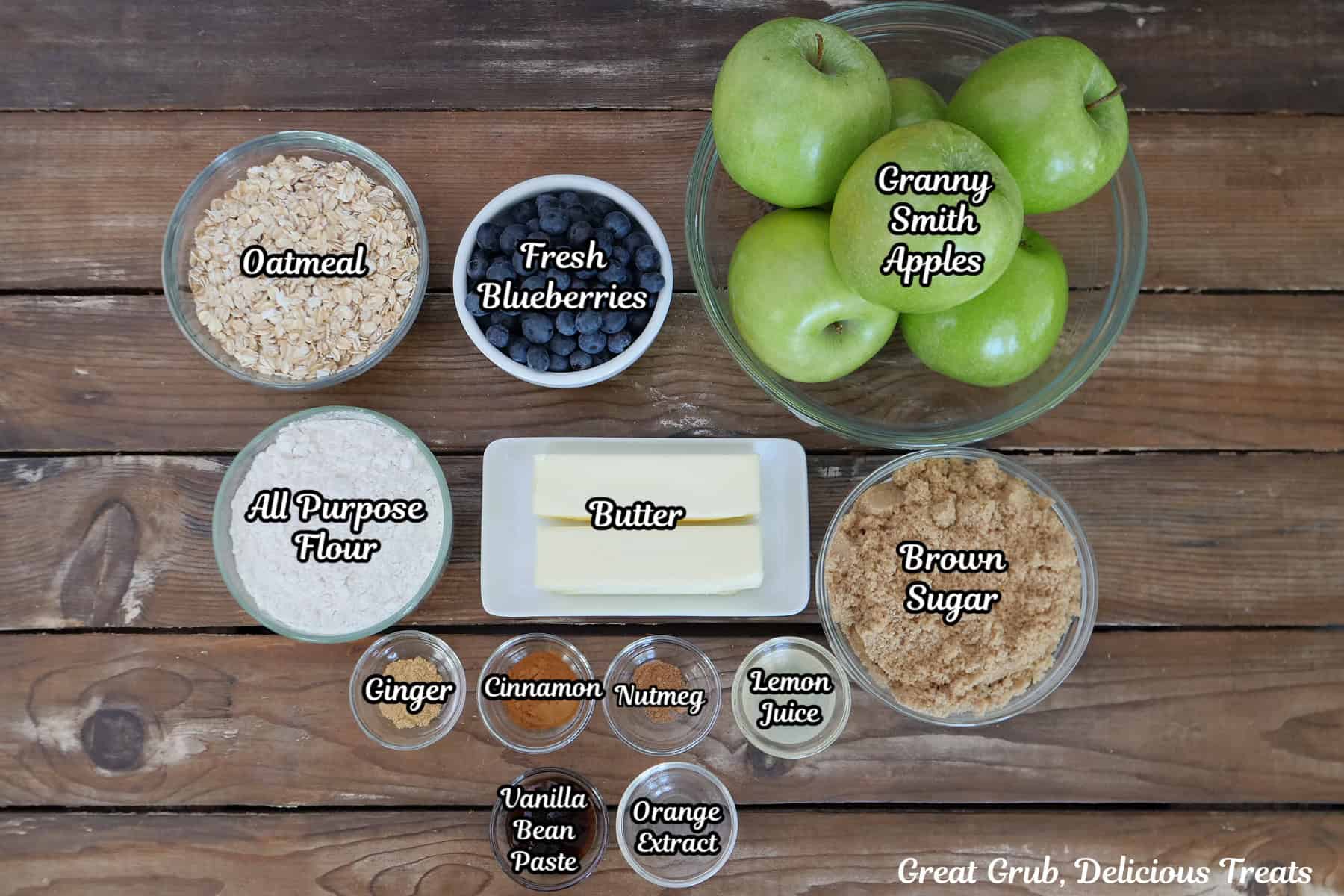 A wood surface with all the ingredients placed on it to make sheet pan apple blueberry crisp.