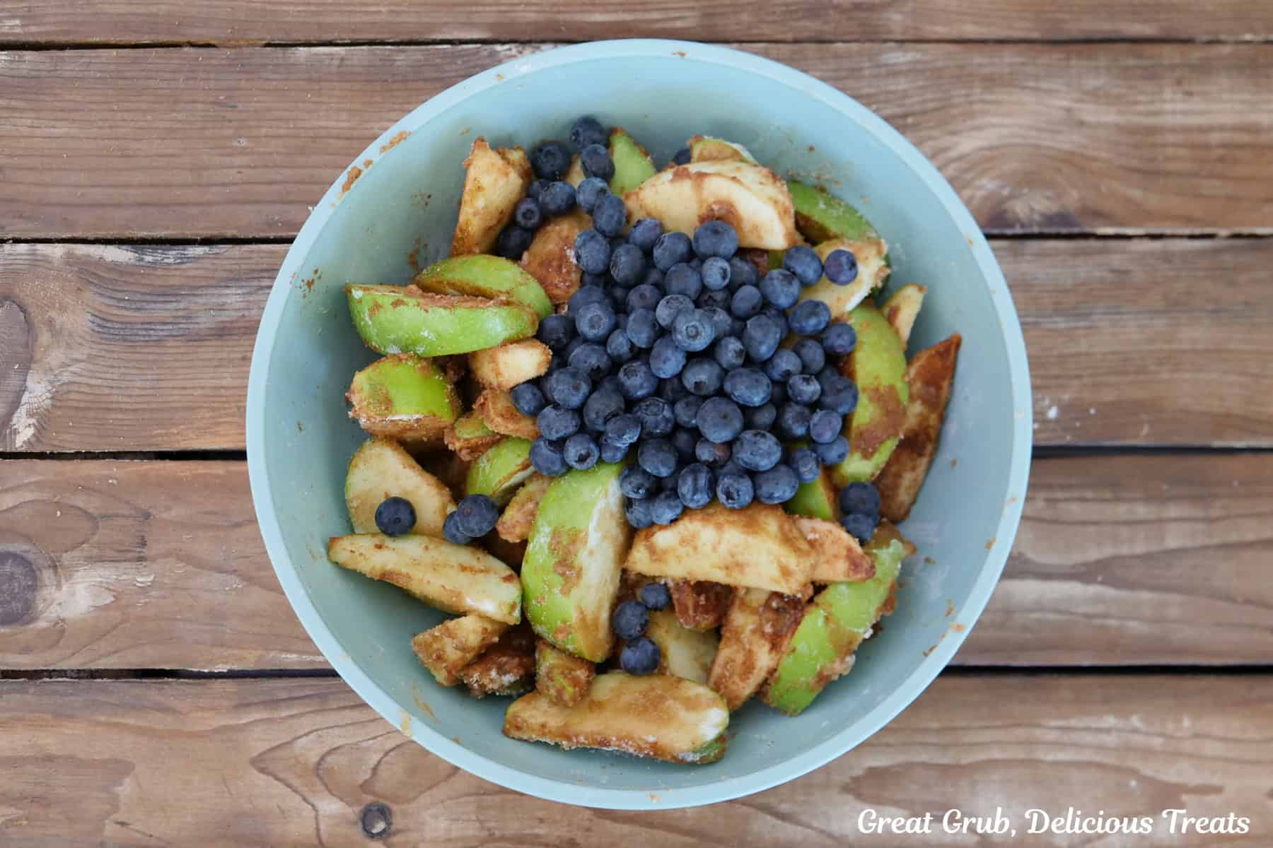 A woos surface with a light blue bowl filled with sliced green apples and blueberries.