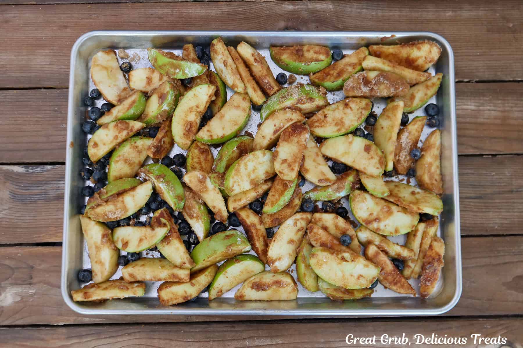 A baking sheet placed on a wood surface with an apple and blueberry mixture spread evenly out on it.
