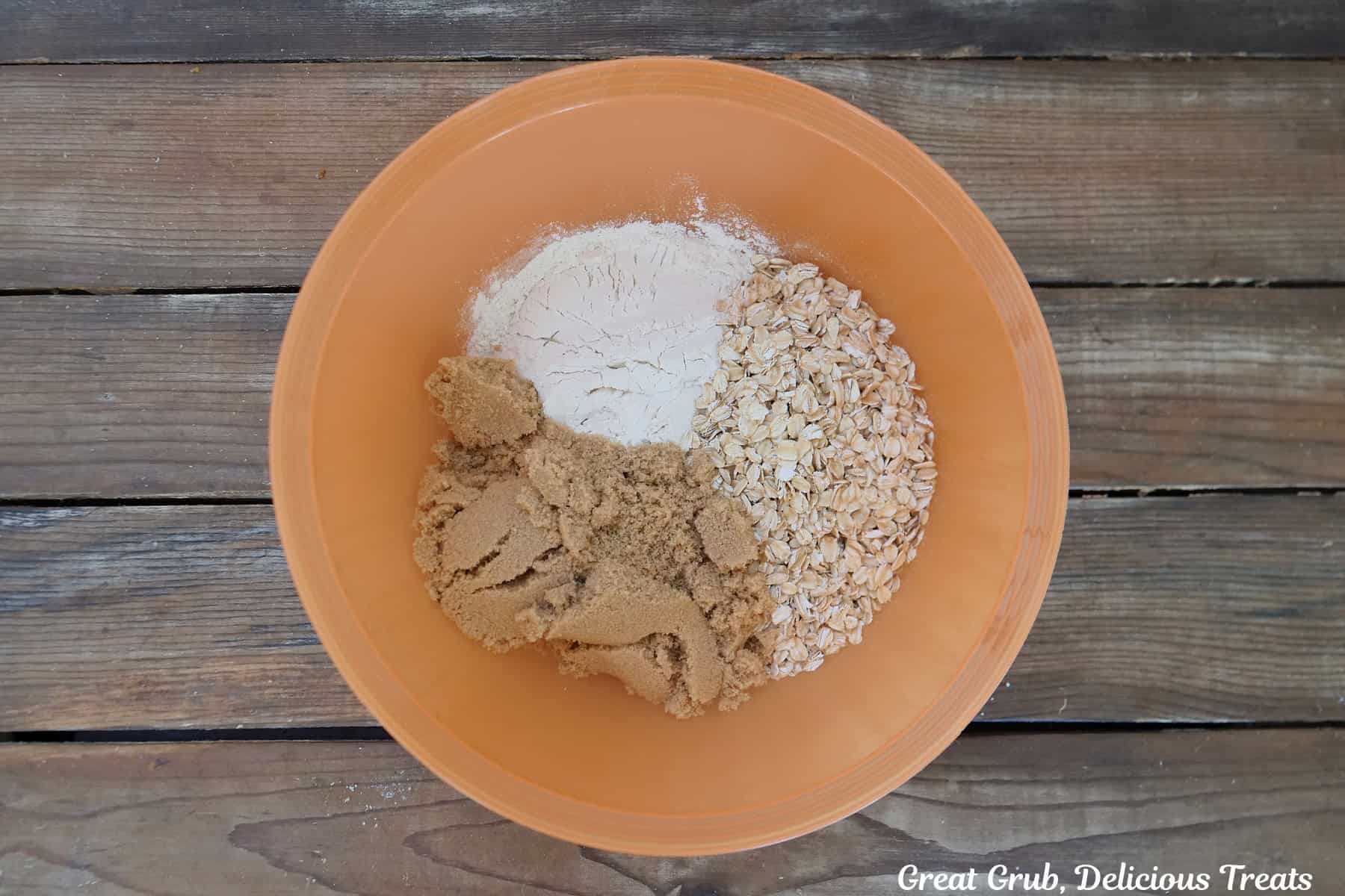 A wood surface with an orange bowl filled with crisp topping ingredients before being mixed together.