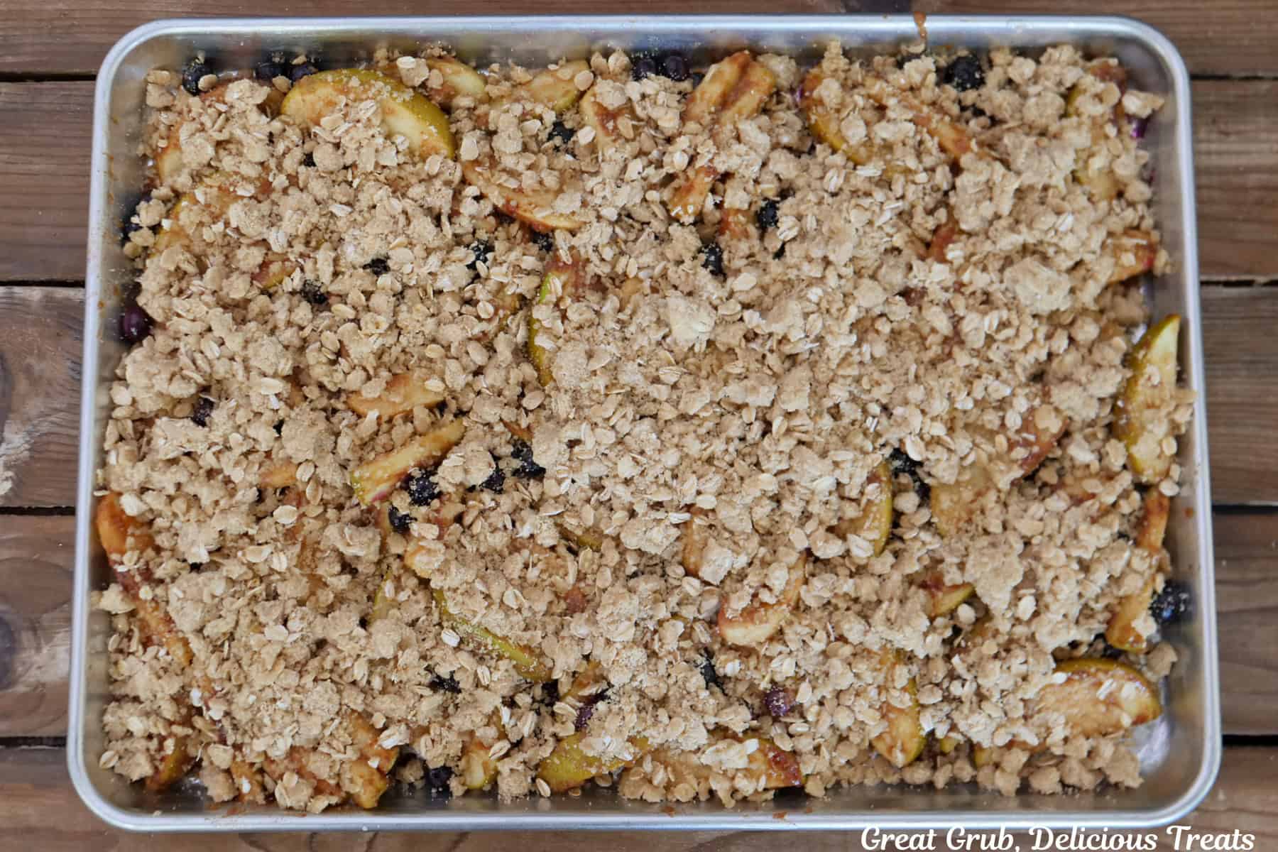 A baking sheet with a crisp topping spread over apples and blueberries before being baked in the oven.
