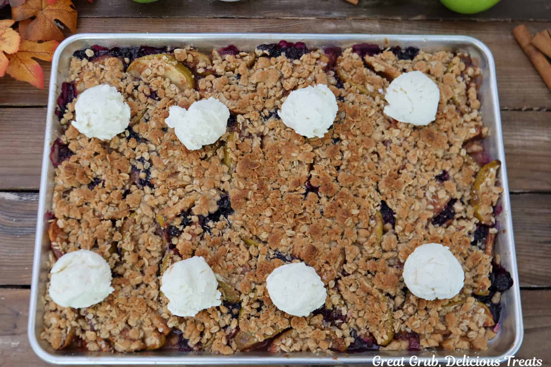 Sheet pan apple blueberry crisp with eight scoops of vanilla ice cream on top.