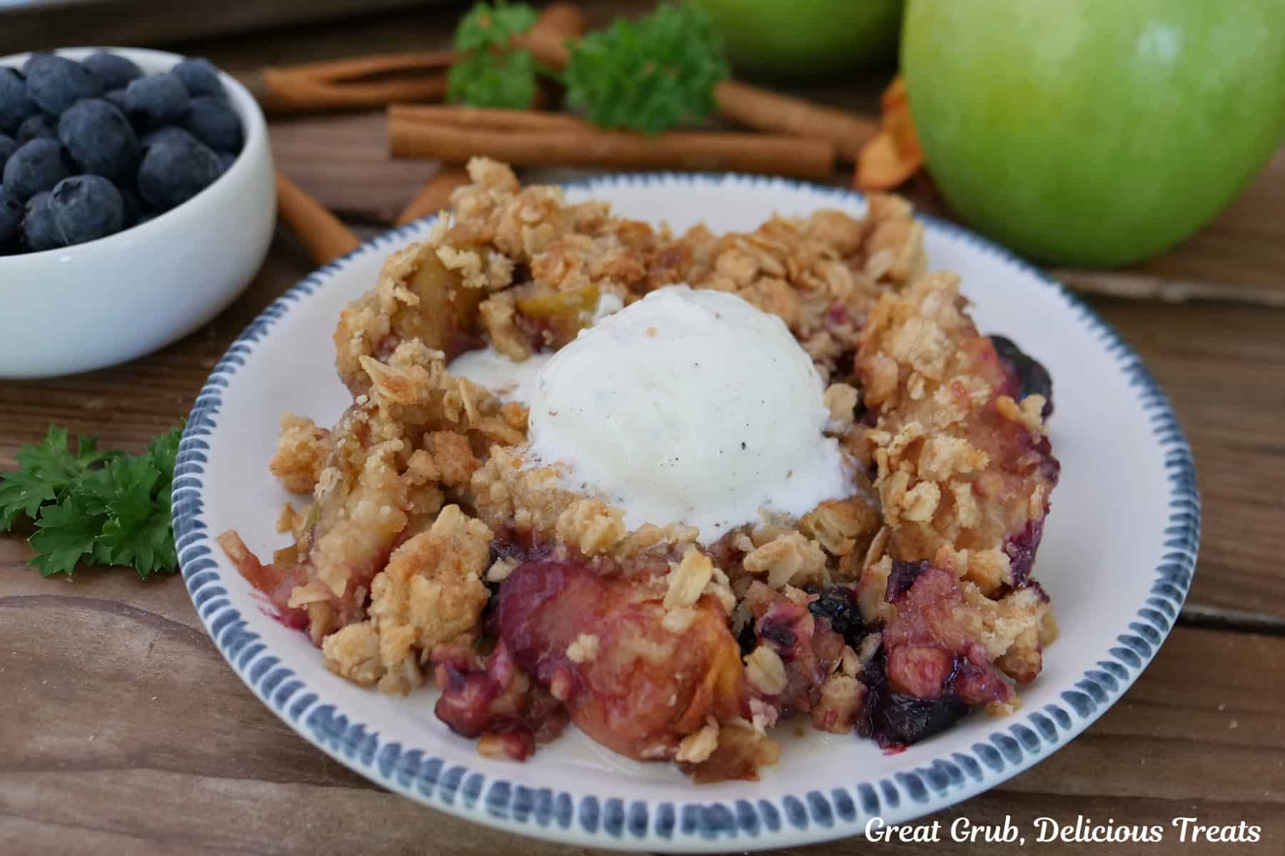 A white bowl with blue trim with a serving of sheet pan apple blueberry crisp on it.