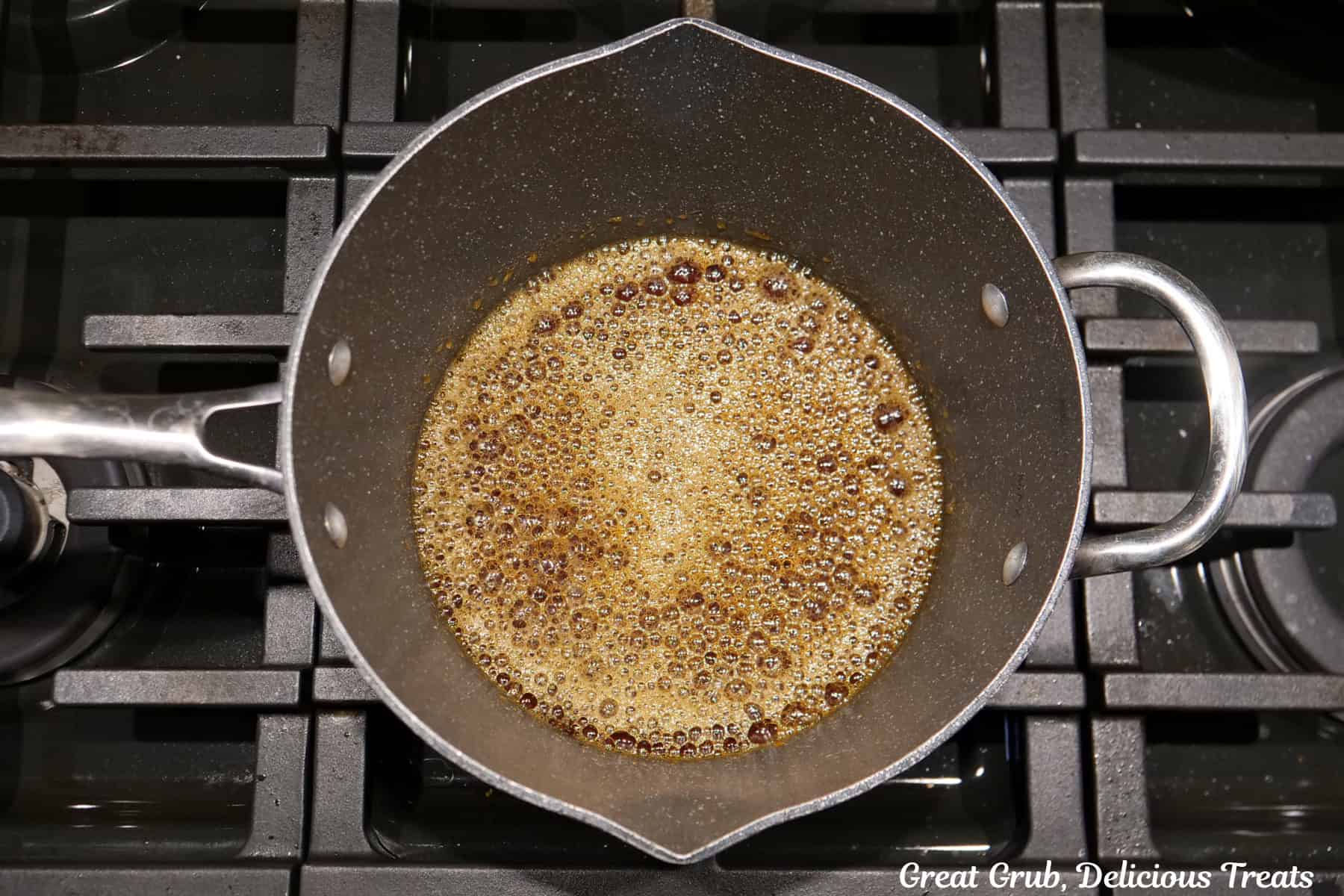 A saucepan on the stovetop with the start of caramel cooking, the sugar and water.