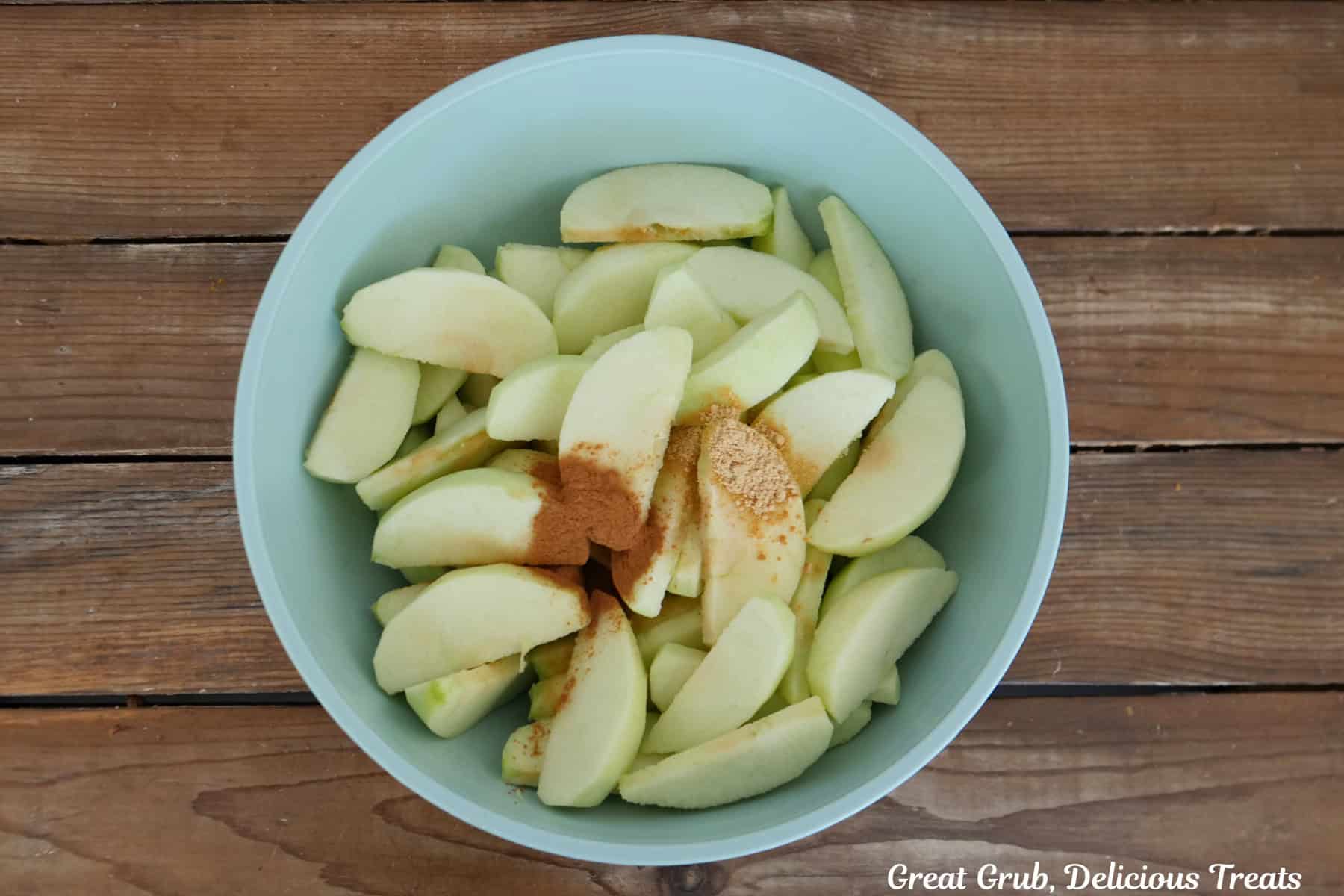 A light blue mixing bowl with sliced apples, cinnamon, ginger, and lemon juice added.