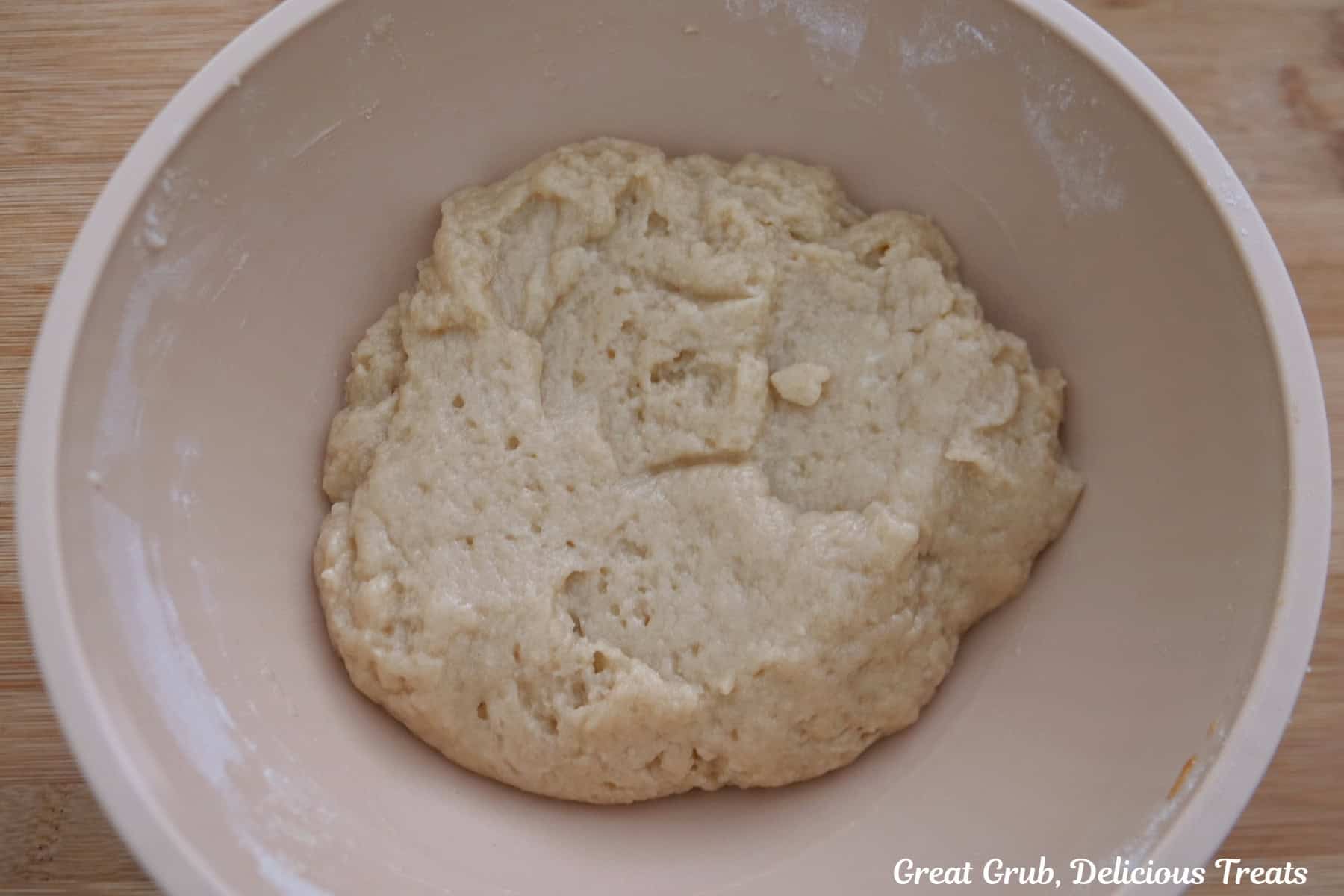 A light colored mixing bowl with peach cobbler topping mixed together.