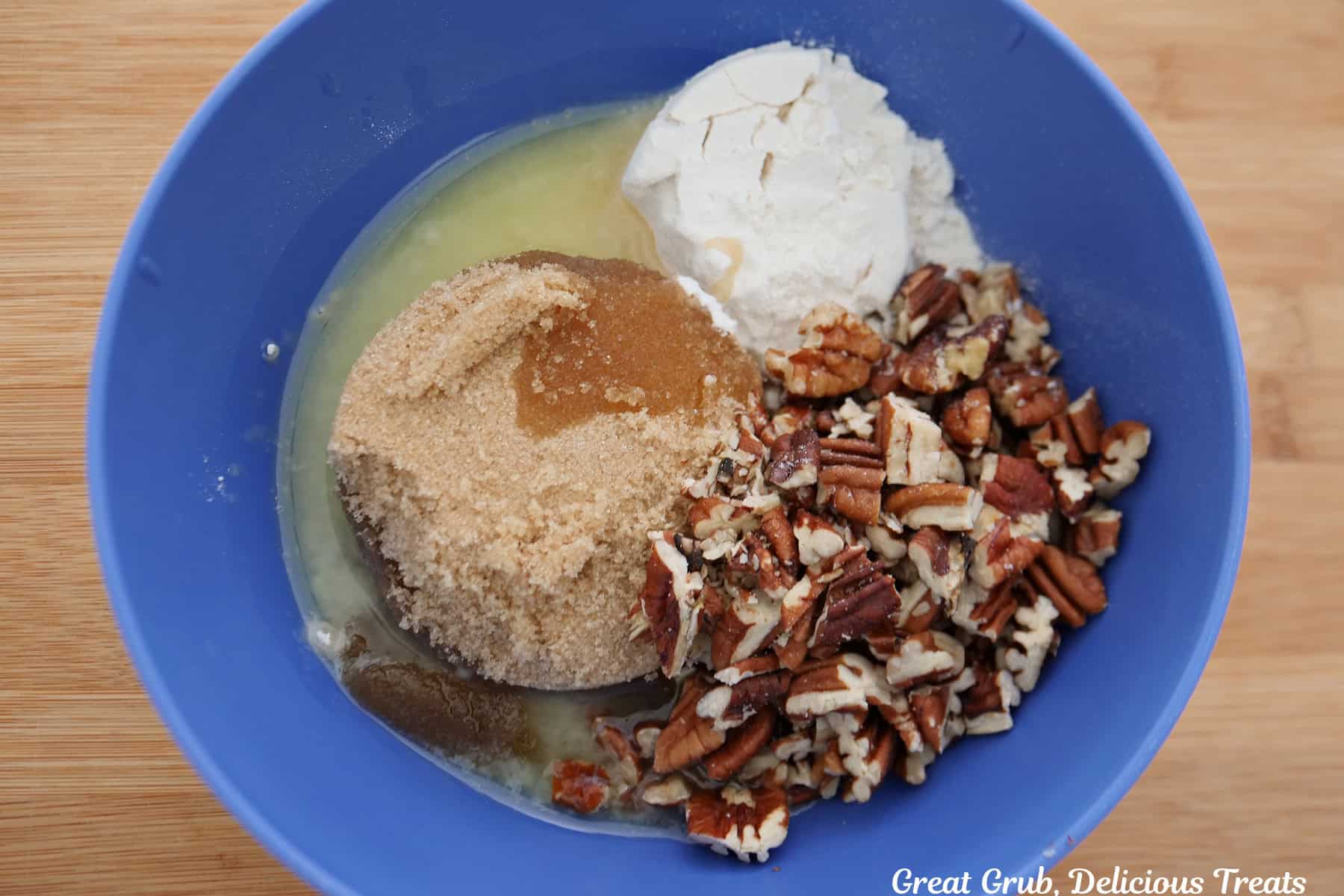 A blue bowl filled with chopped pecans, brown sugar, flour, and melted butter in it before being mixed together.
