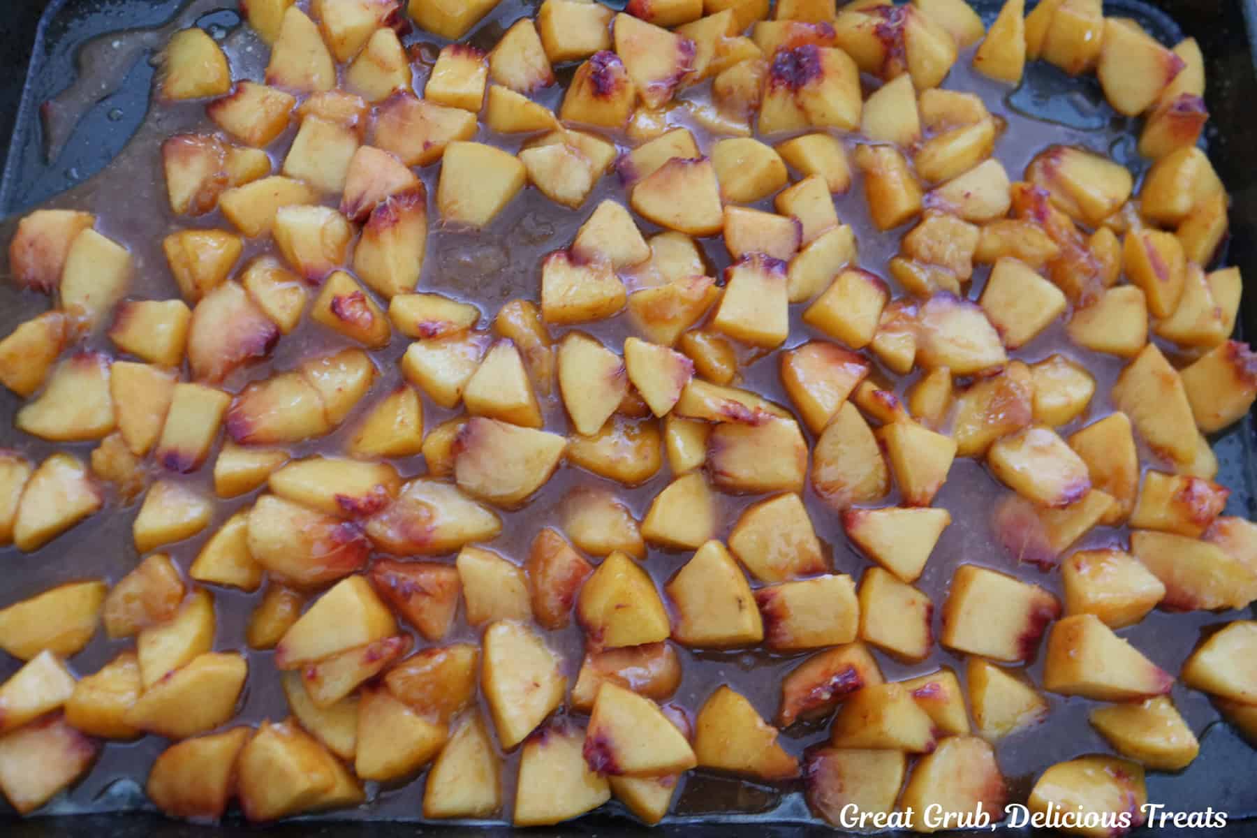 A baking sheet with the peach cobbler filling ingredients spread out in an even layer.