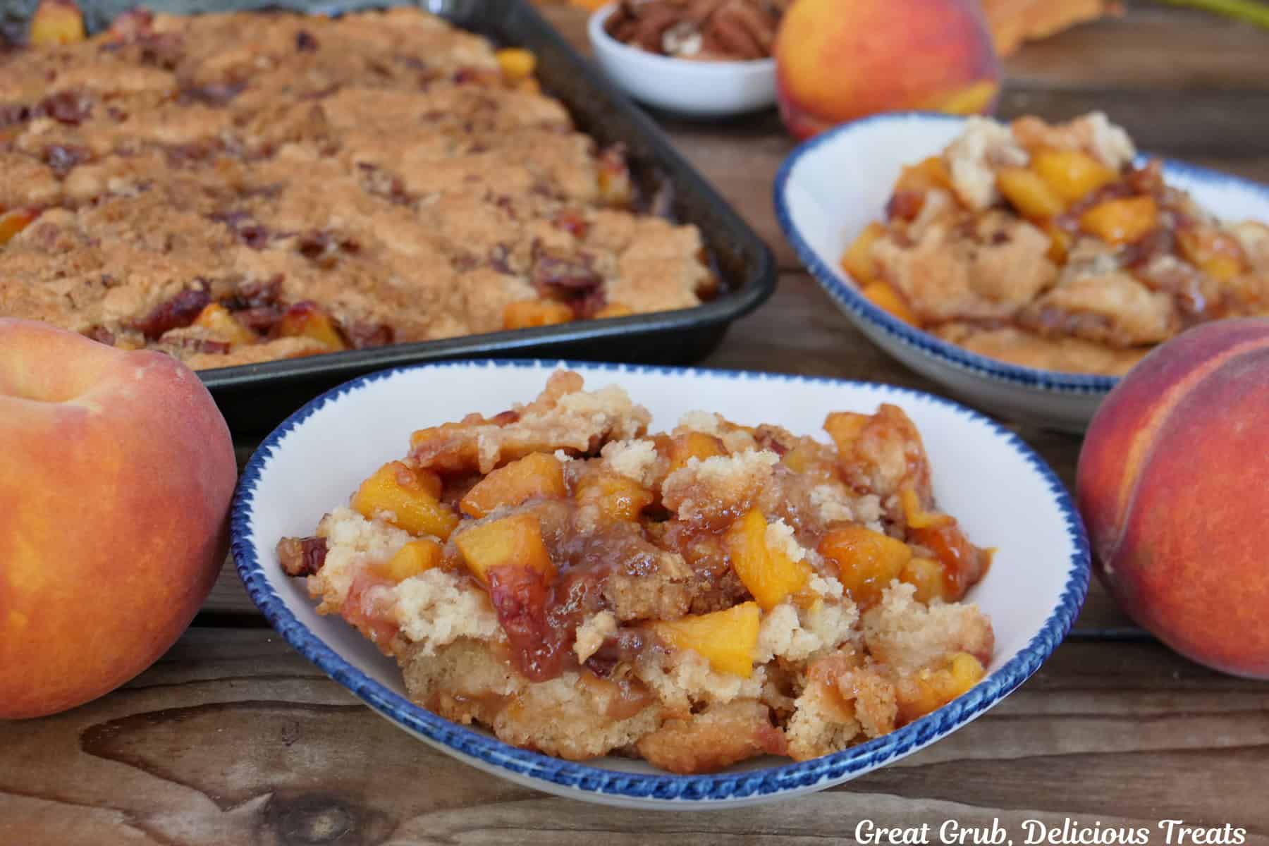 A white bowl with blue trim with a serving of peach cobbler in it with a sheet pan filled with peach cobbler in the background.