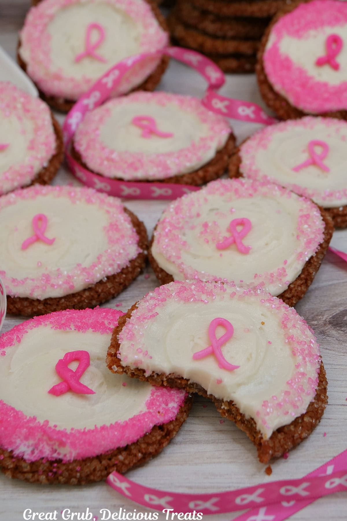 A white surface with nine molasses frosting cookies on it with a bite taken out of the cookie in front.