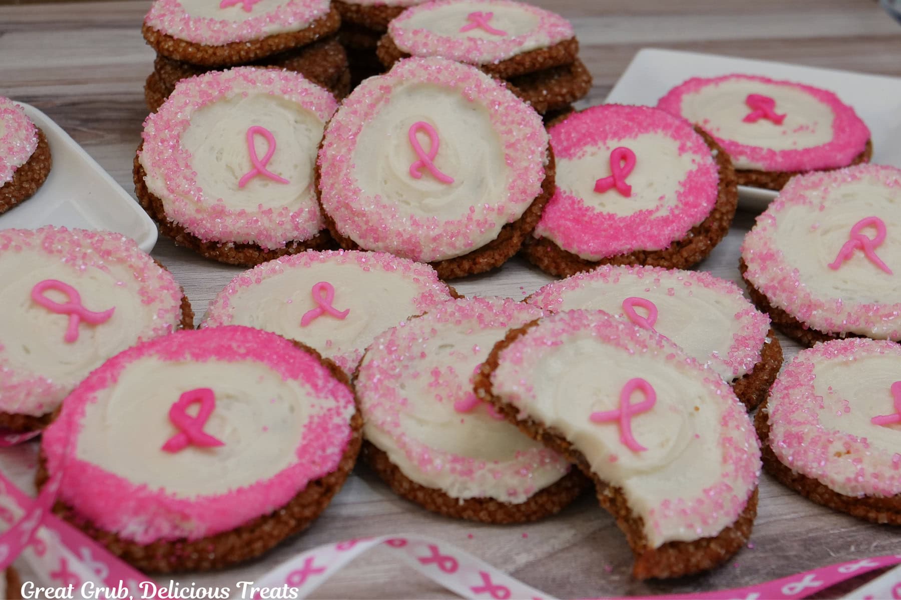 Frosted molasses cookies representing breast cancer awareness scattered around on a white surface, with a bite taken out of the cookie in front.