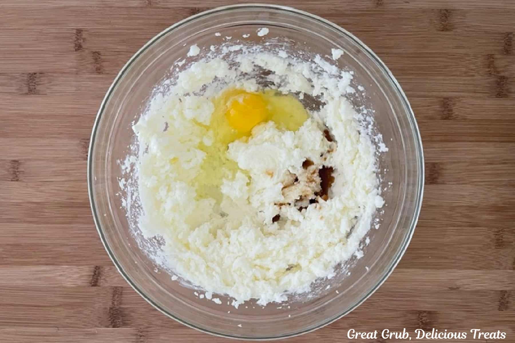 A wood surface with a glass bowl filled with the wet cookie ingredients for sugar cookies before being mixed together.