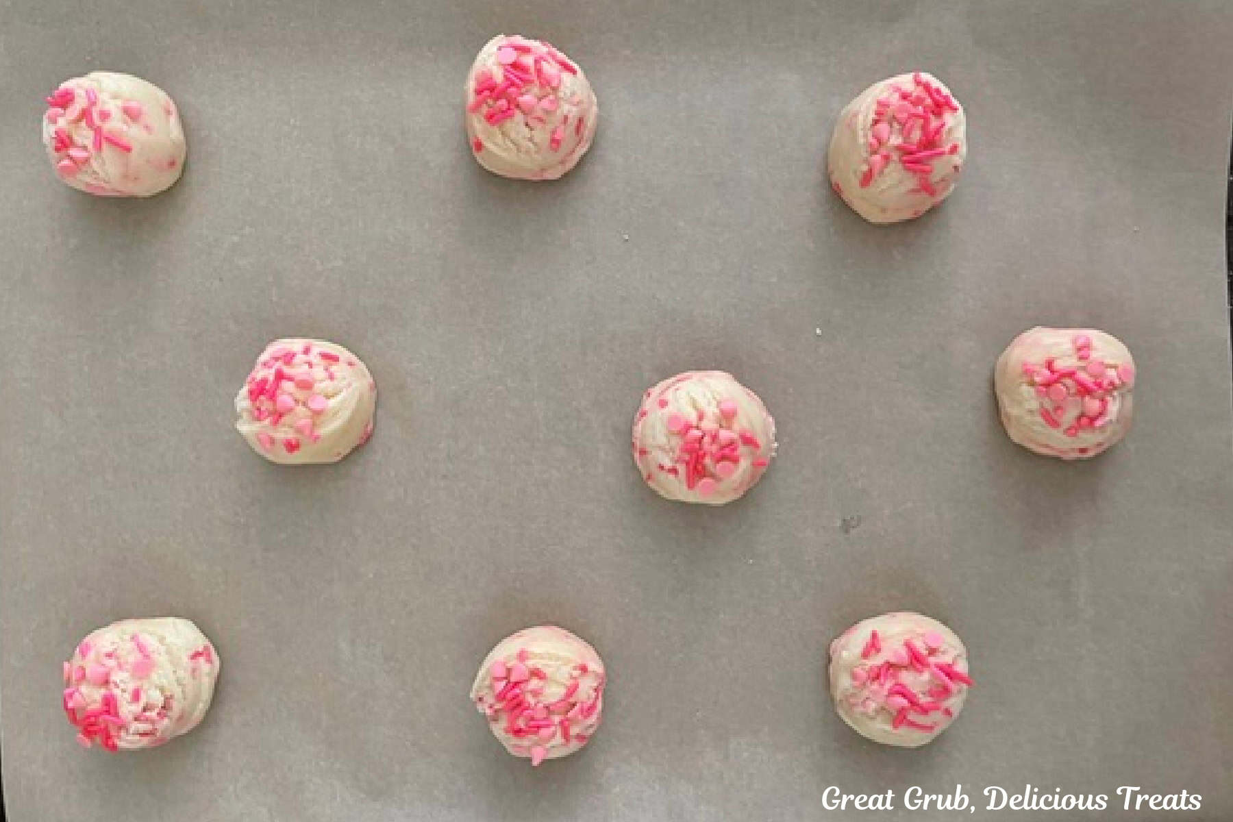 A parchment lined baking sheet with nine sugar cookie dough balls on it before being baked.