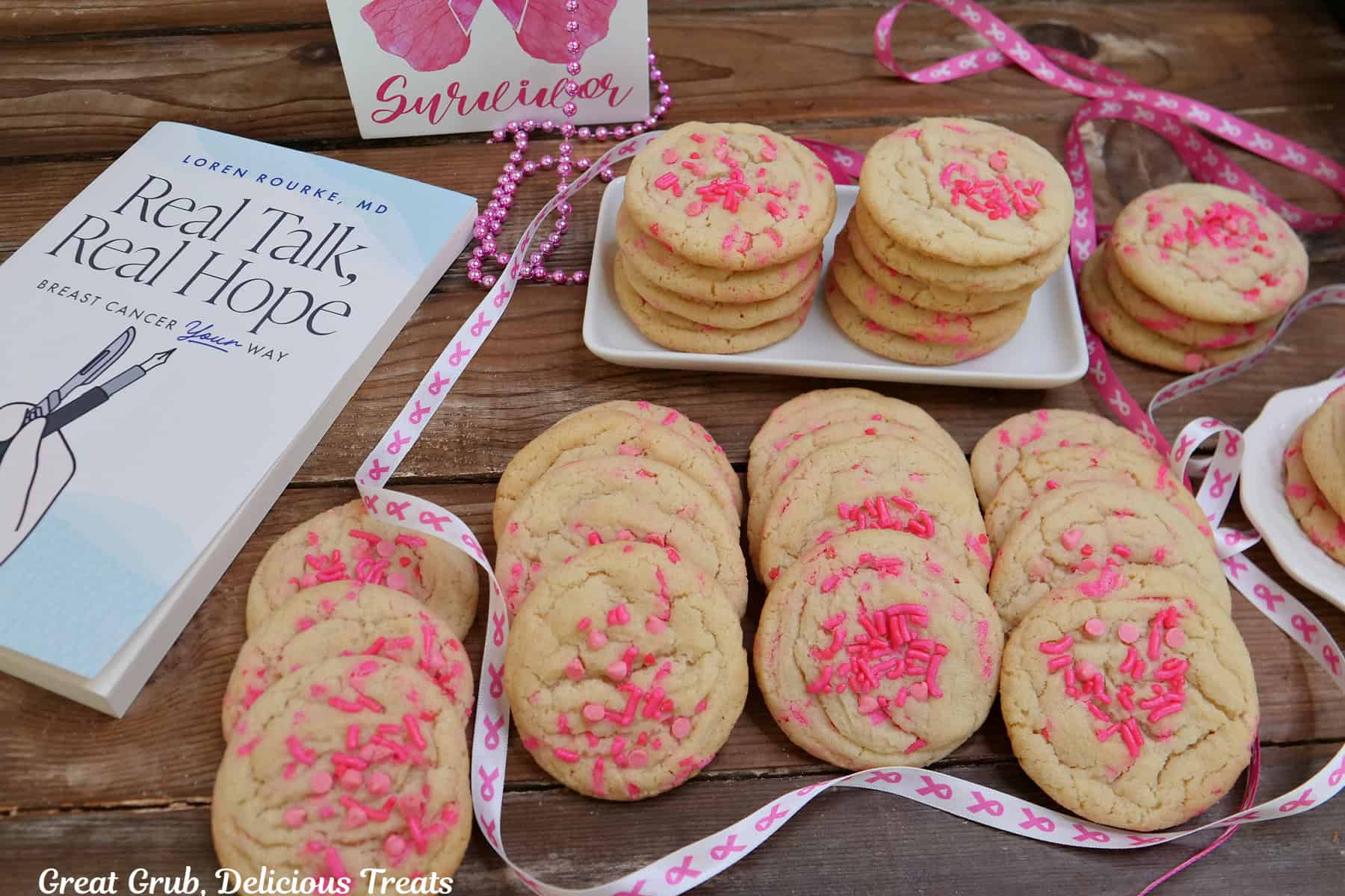 A wood surface with with two dozen breast cancer sugar cookies on it with Dr. Rourke's Real Talk, Real Hope book in the background.