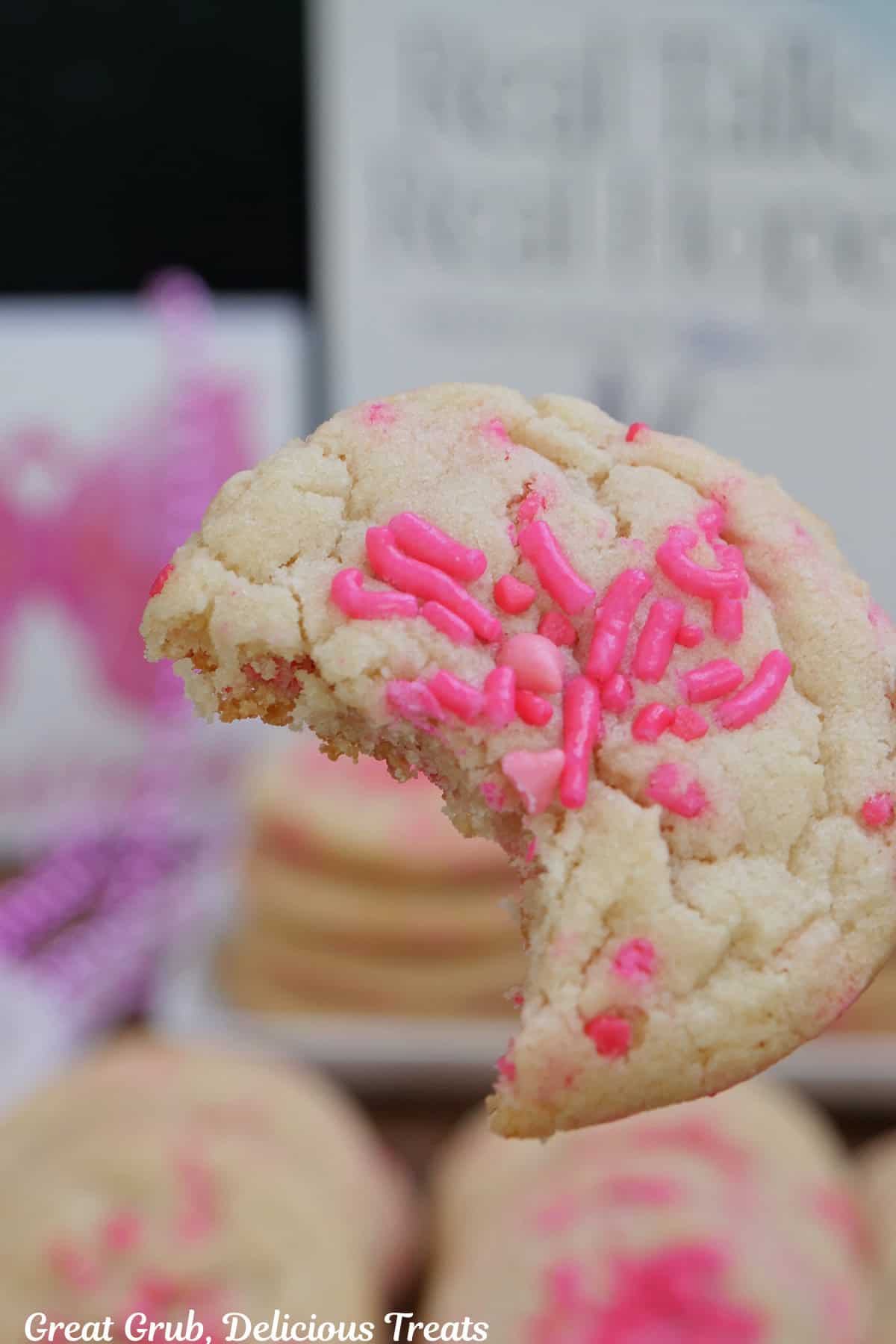 A sugar cookie, held up above other cookies, with a bite taken out of it.