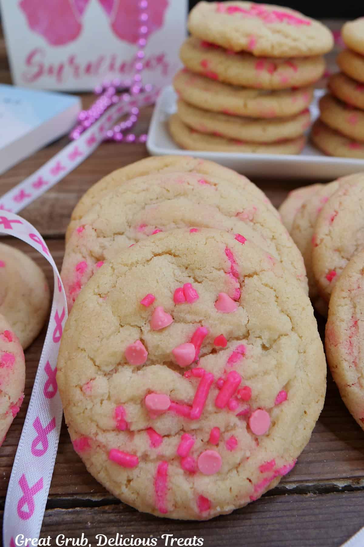 A row of breast cancer sugar cookies placed on a wood surface with more cookies in the background.