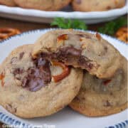 A white round plate with blue trim with four brown butter pretzel toffee cookies on it with a bite out of the cookie on top.